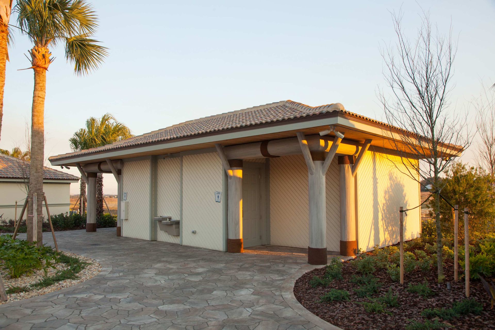 Outdoor restroom or storage building with a tile roof and palm trees.
