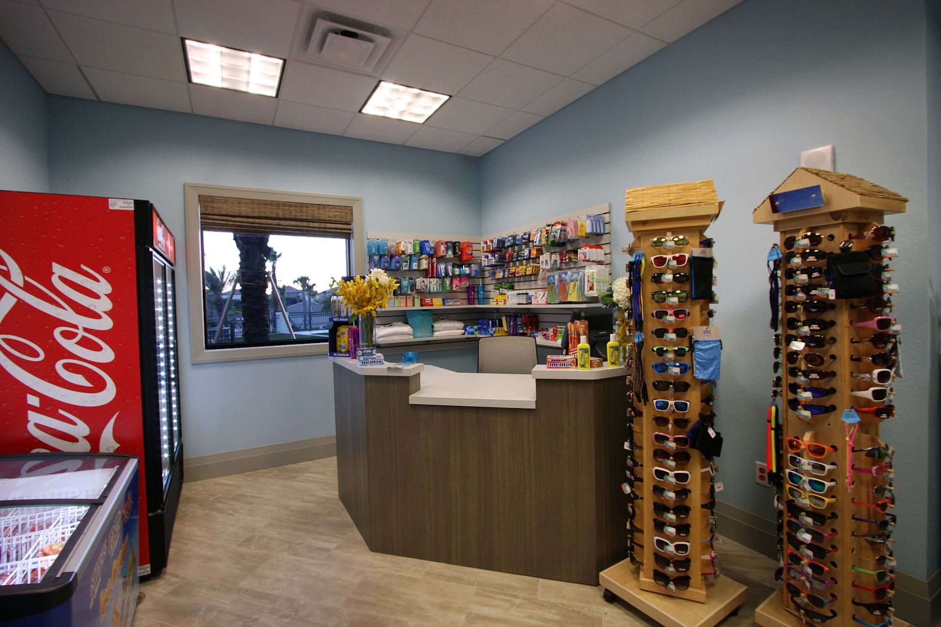 Resort snack bar or sundry shop with a counter, fridge, and sunglasses display.