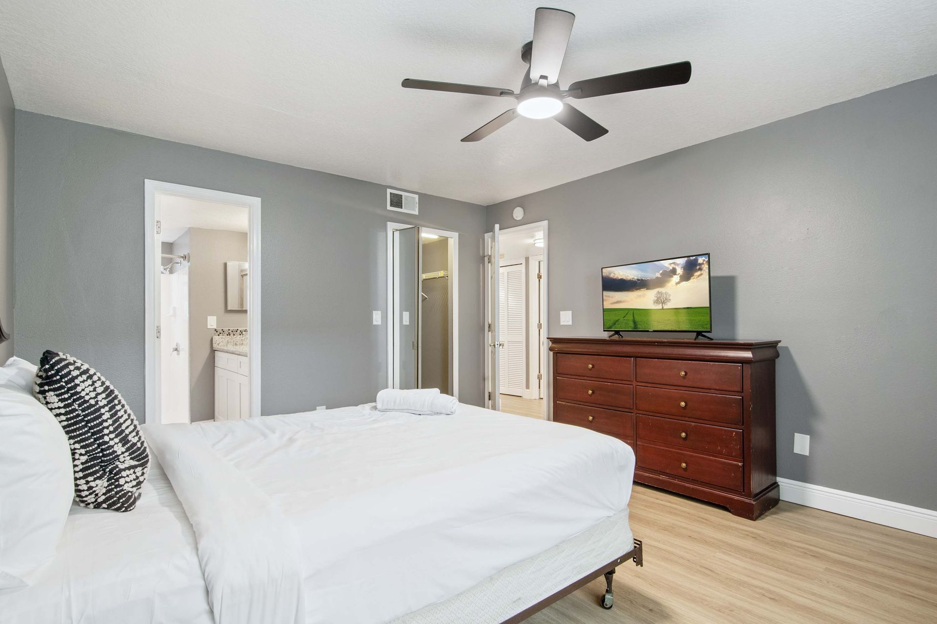Queen bedroom with modern gray walls and rich wood dresser/TV. 