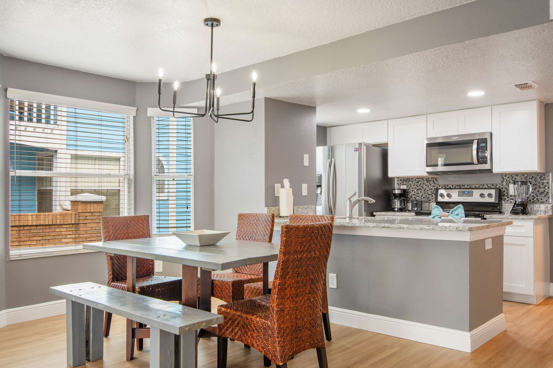 Modern dining with woven chairs, open to a sleek white kitchen. 