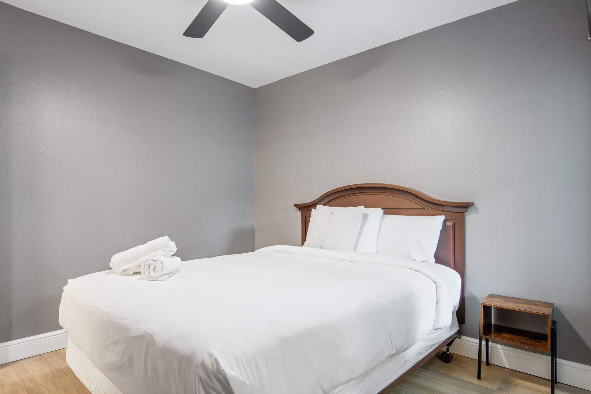Minimalist queen room with warm wood accents and dark gray walls.