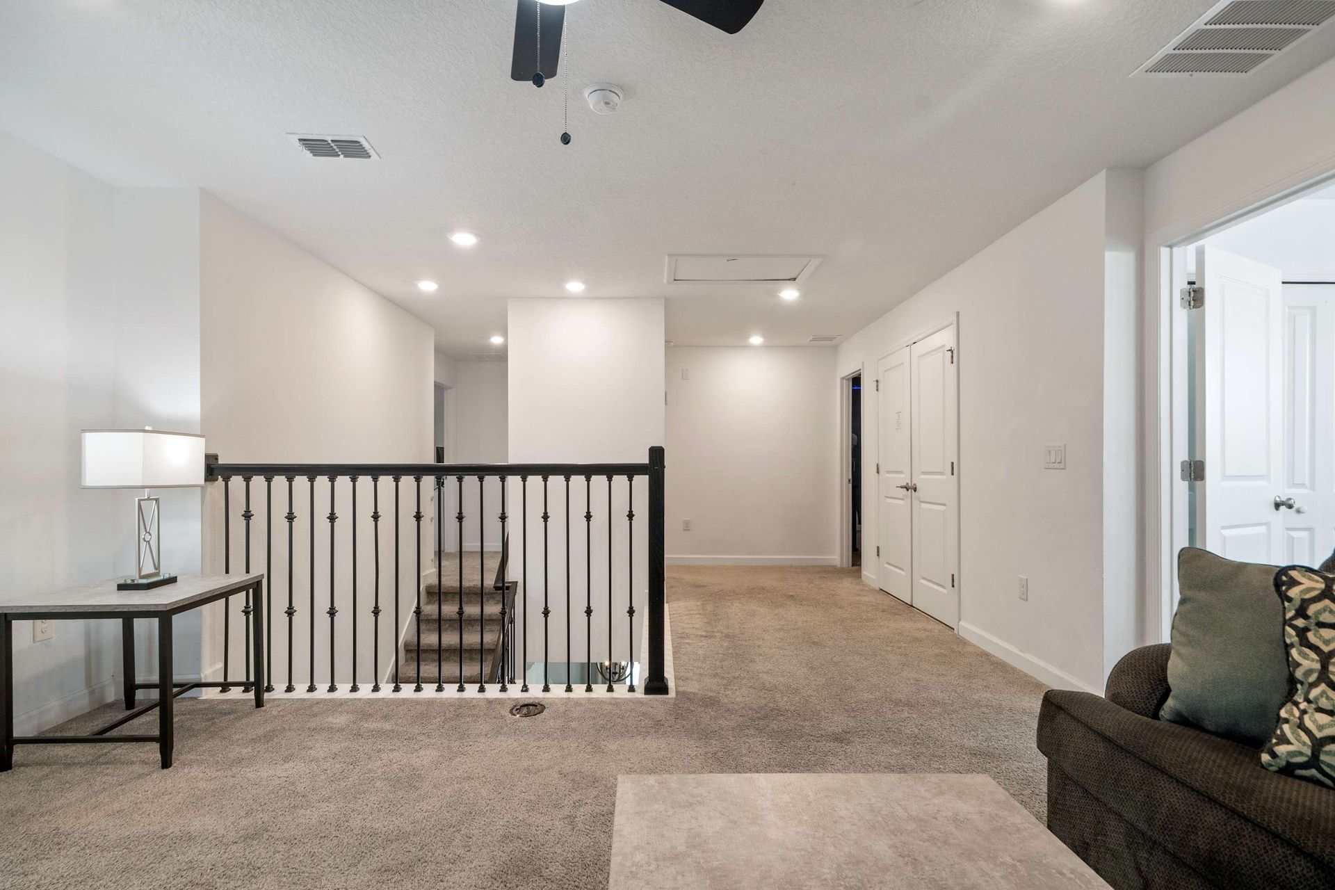Spacious carpeted loft area with railing and recessed lighting.