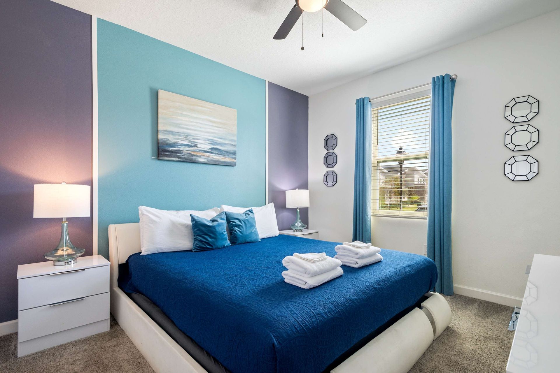 Vibrant blue and purple walls with a cozy queen bed and ocean art.