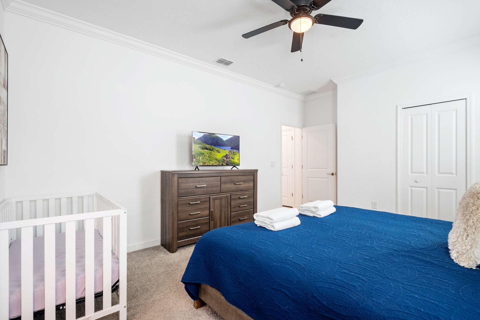 Cozy queen bed, TV, and crib in a clean, sunlit bedroom. 