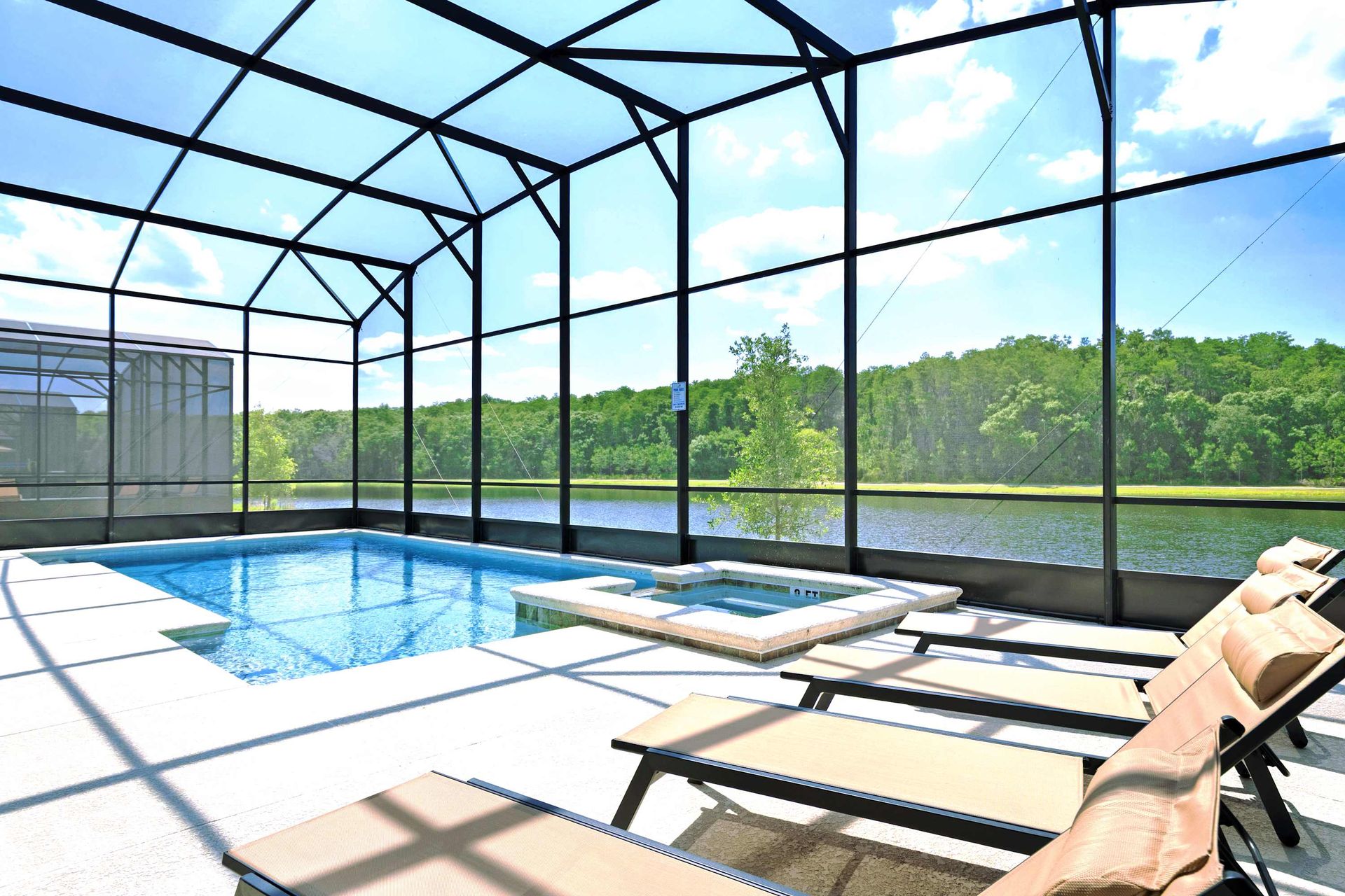 Screened pool and spa with sun loungers and a serene lake view.