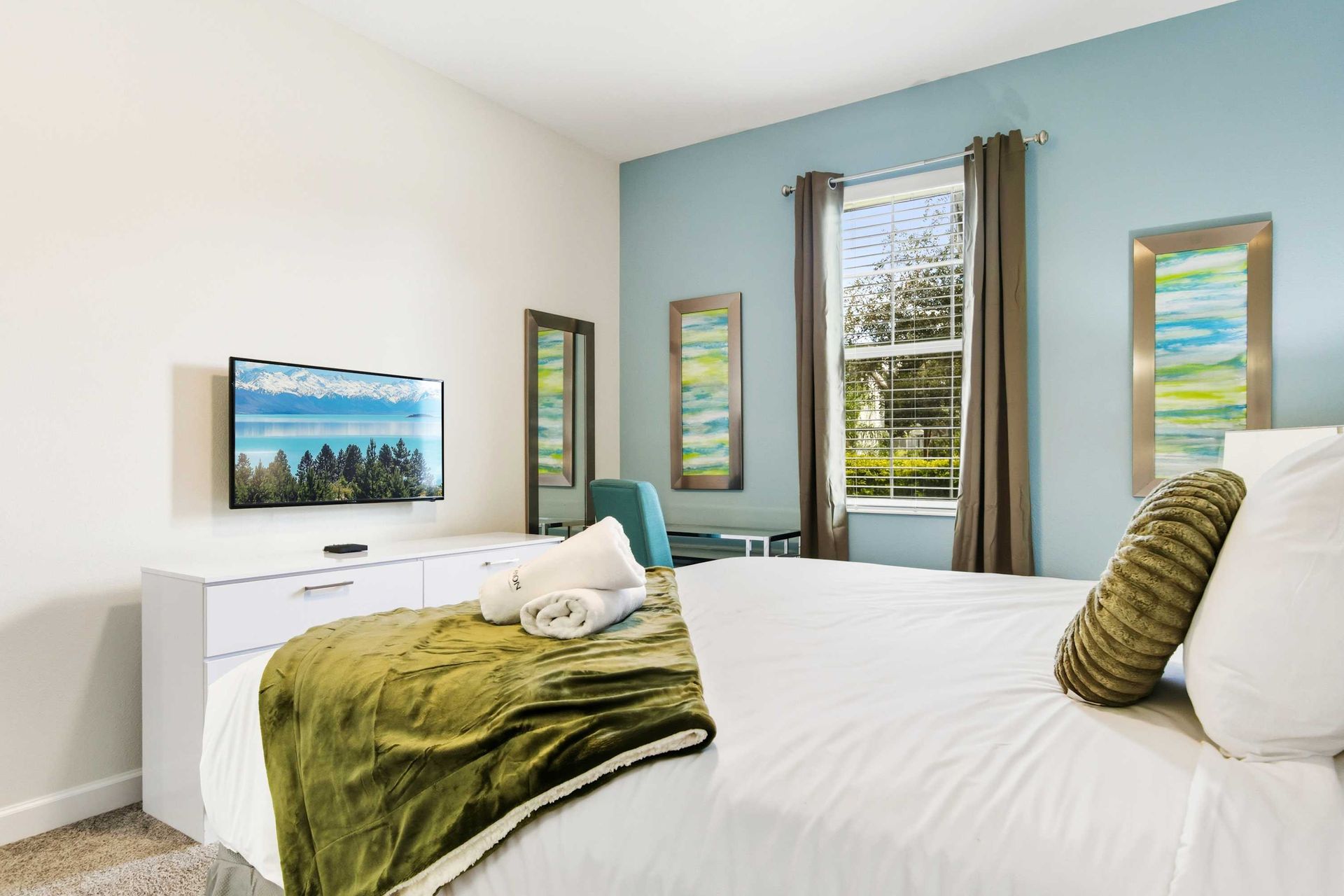 Spacious, serene master suite with chic white furniture and huge TV.