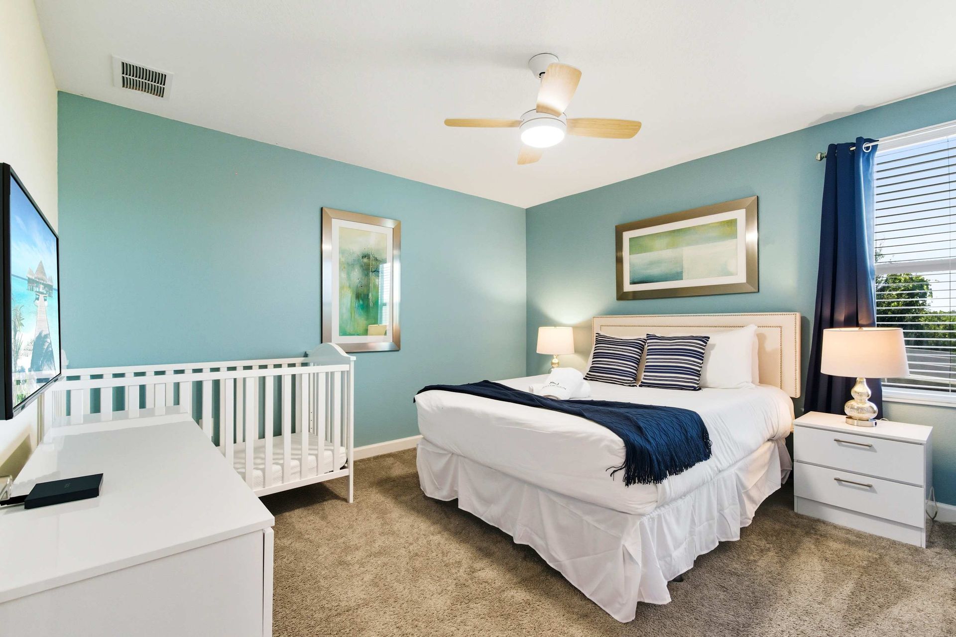 Coastal-inspired bedroom with ceiling fan and convenient crib.