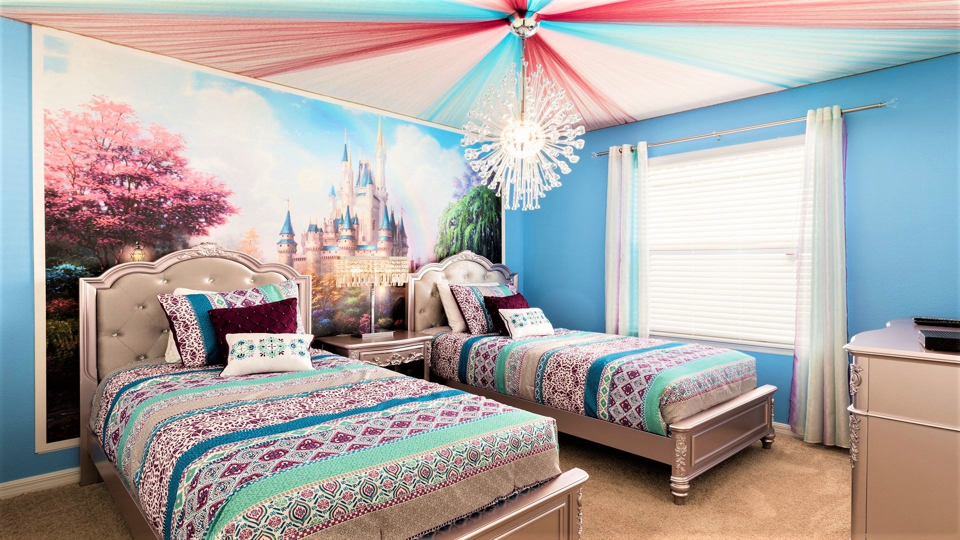 Whimsical princess-themed bedroom with twin beds, castle mural, and colorful canopy ceiling.
