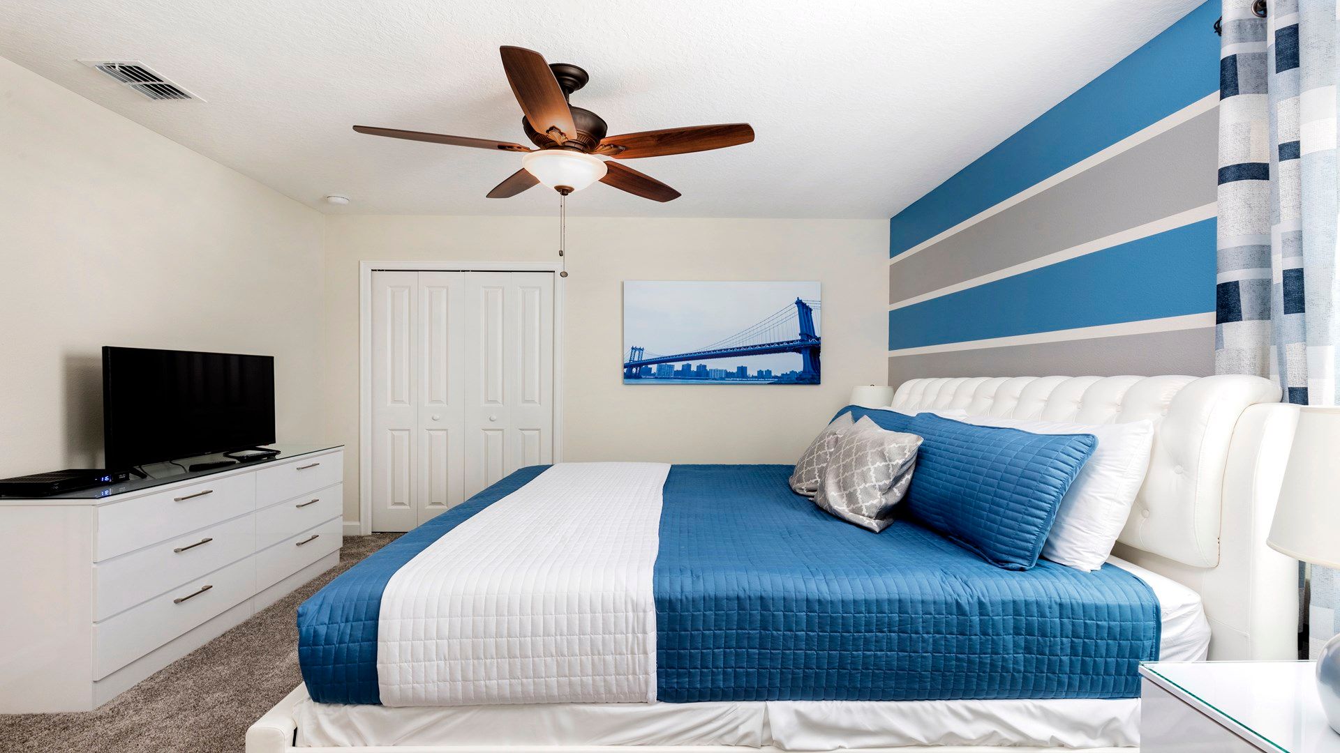 Chic bedroom with king bed, striped accent wall, and smart TV