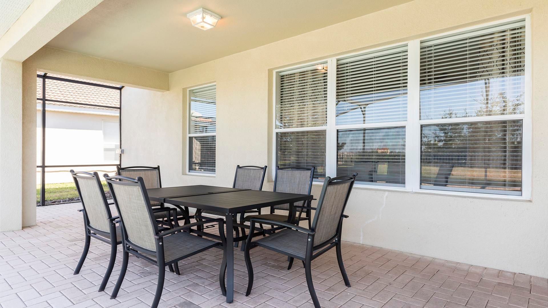 Covered lanai with comfortable dining set, ideal for outdoor meals and relaxation.