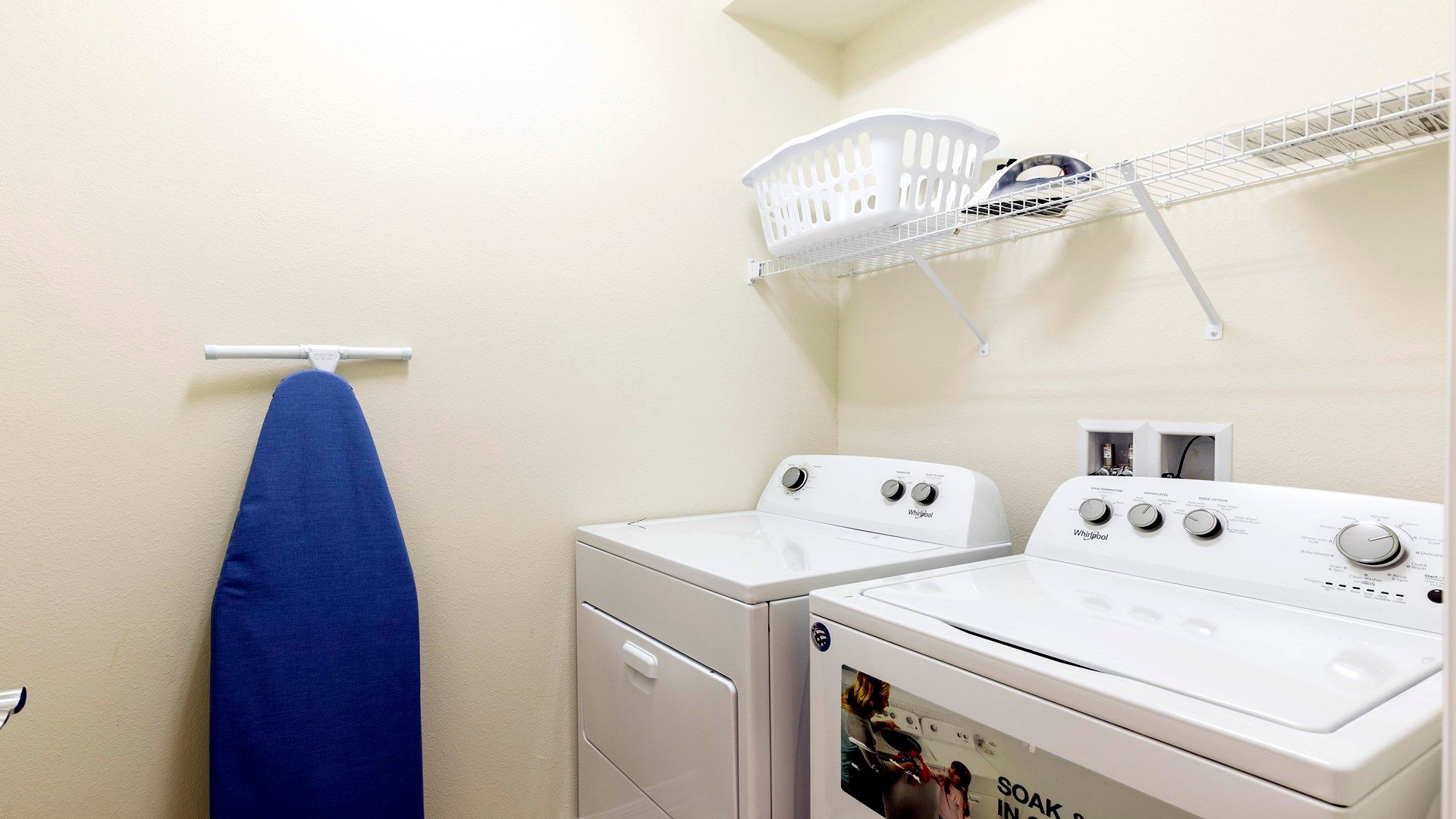 Convenient laundry room with washer, dryer, ironing board, and ample shelving.