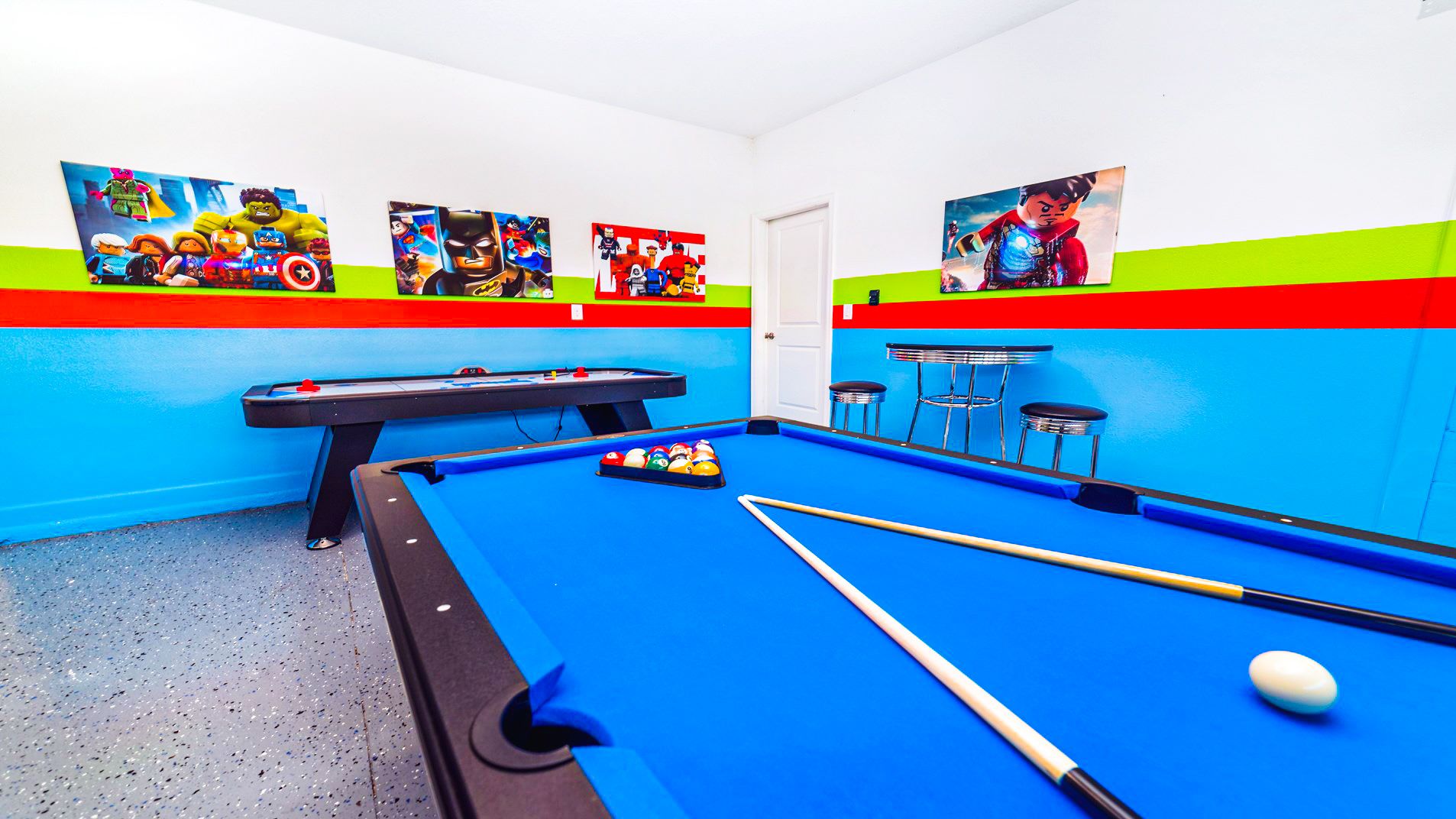 Colorful game room with a blue pool table, air hockey, and superhero-themed wall art, perfect for fun.