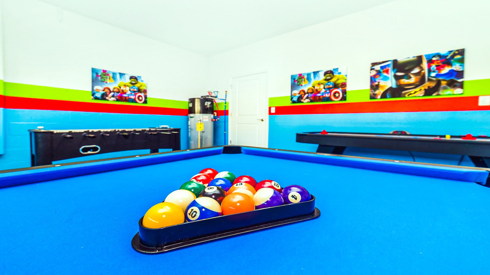 Vibrant game room with superhero-themed decor, featuring a blue pool table, foosball, and air hockey.