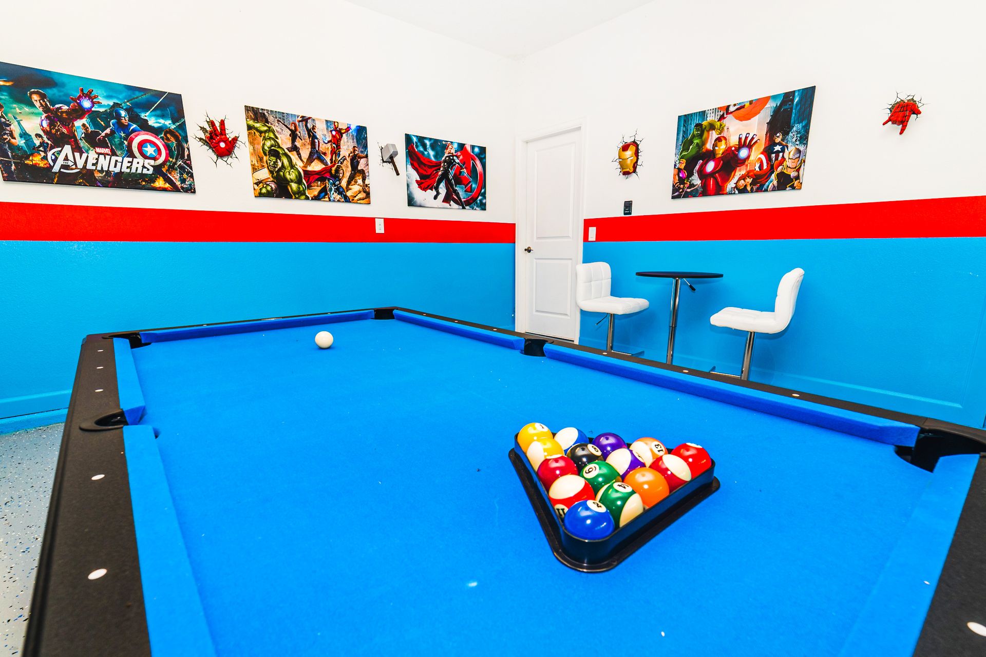 Superhero-themed game room with blue pool table, Avengers posters, and cozy seating for ultimate fun.