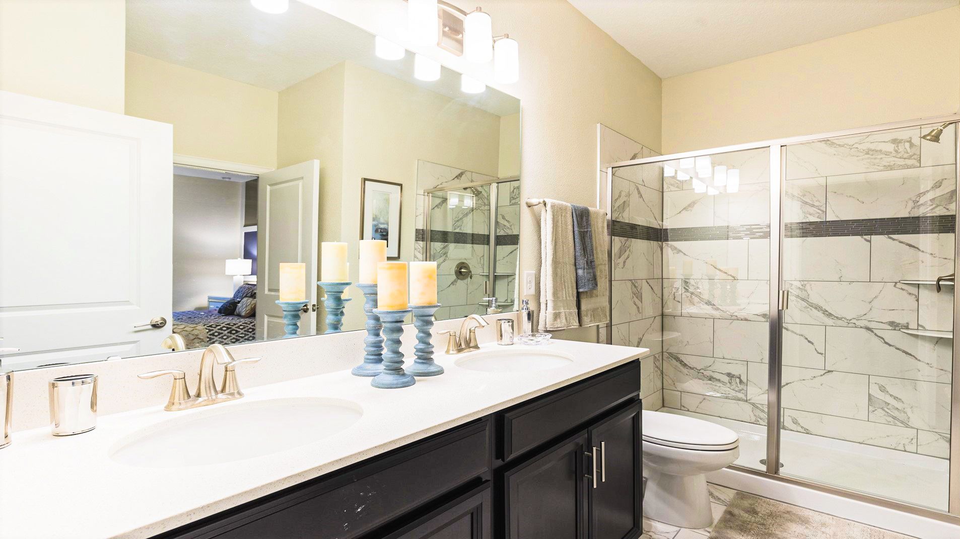 Elegant bathroom with marble-tiled shower, double vanity, and blue candle holders, leading to a cozy bedroom.