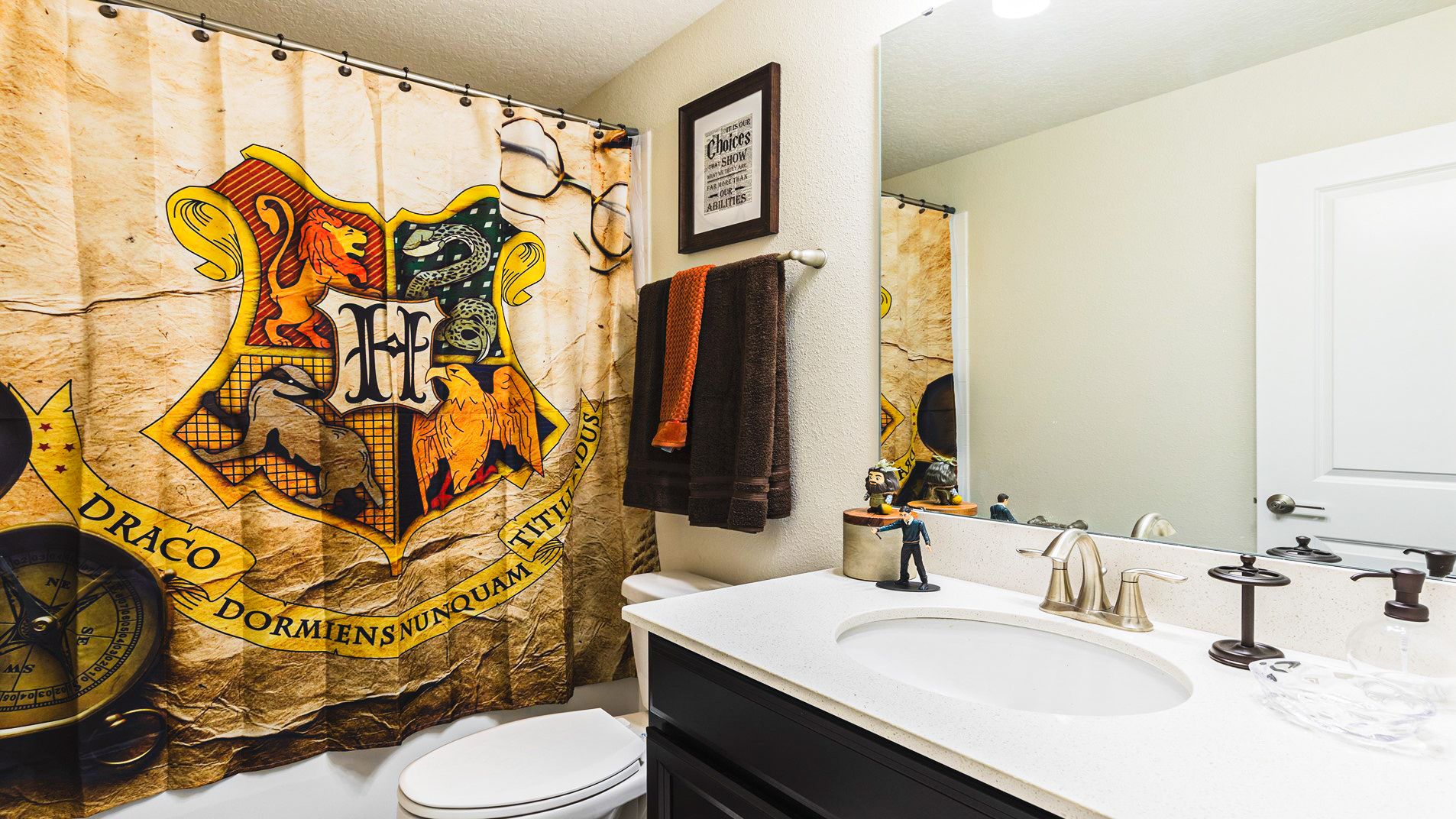 Harry Potter-themed bathroom with Hogwarts shower curtain, Gryffindor and Slytherin towels, and magical decor.
