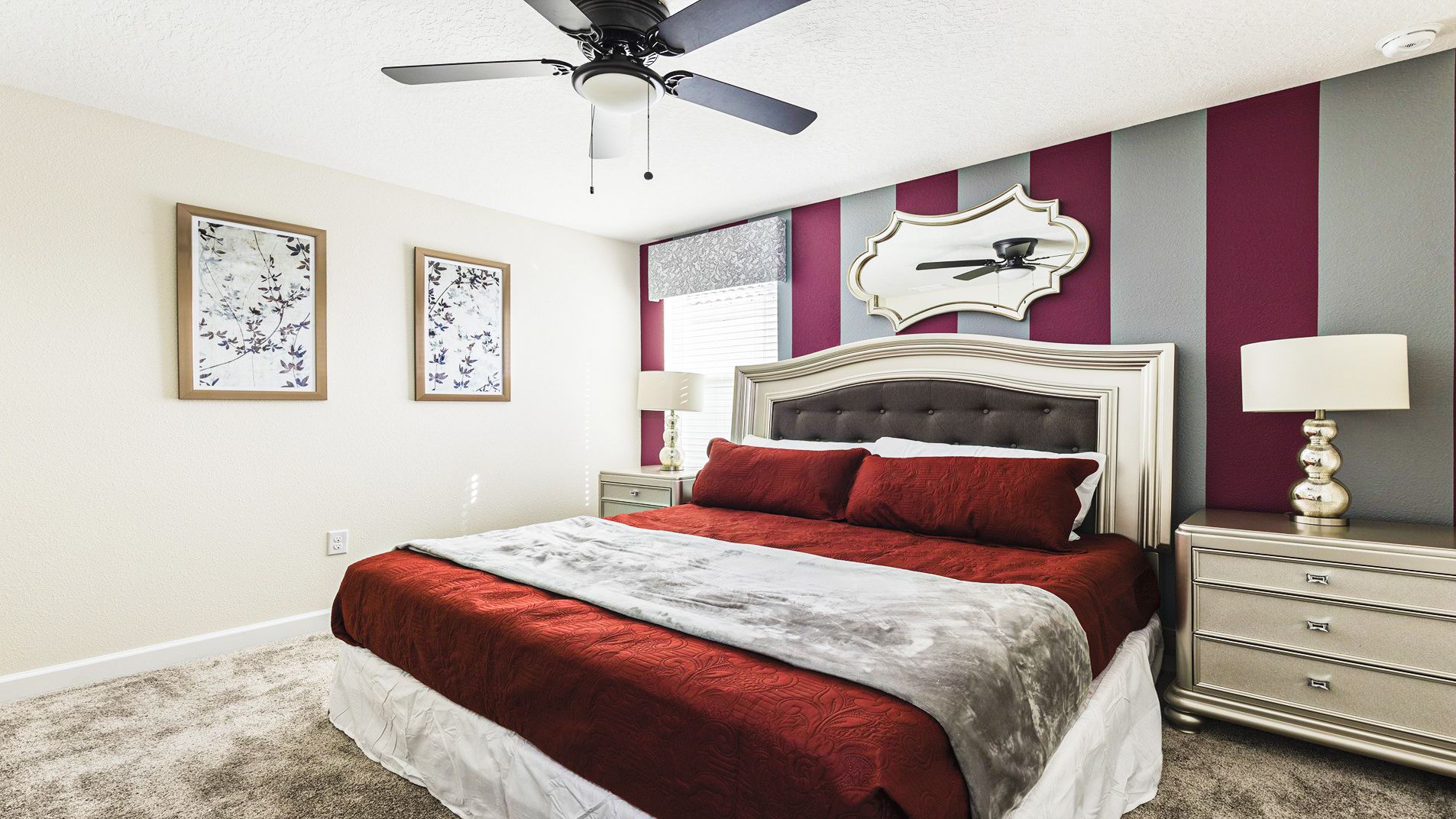 Elegant bedroom with red and gray striped accent wall, luxurious bedding, mirrored decor, and stylish furnishings.
