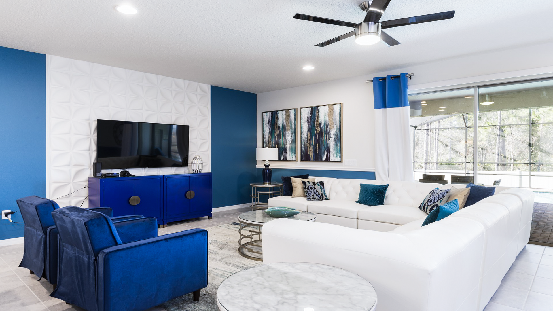 Bright and stylish living room with large TV, plush seating, modern accents, and poolside views.