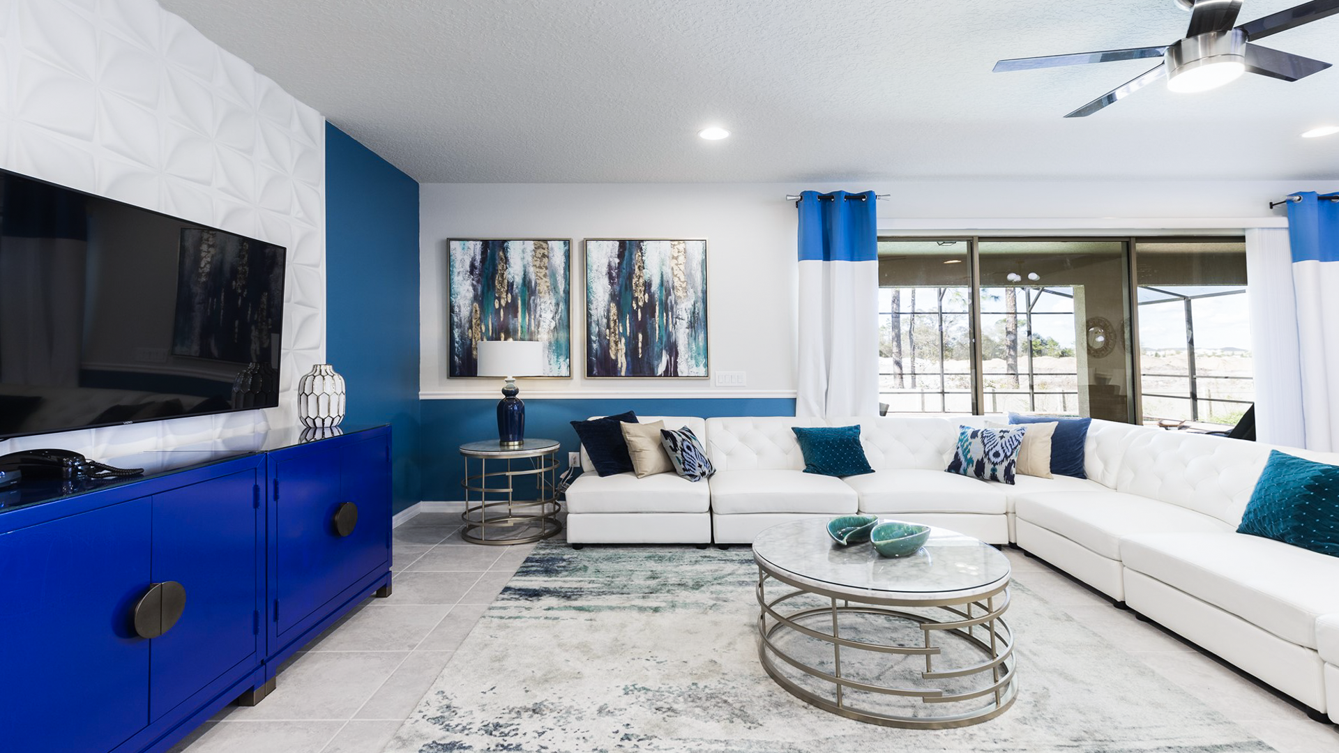 Modern living room with spacious sectional sofa, large TV, chic blue accents, and stylish decor.