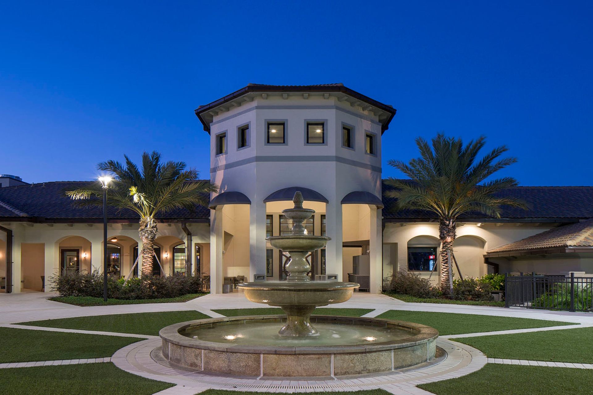 Elegant clubhouse with a grand fountain, palm trees, and beautifully lit paths for a serene evening ambiance.