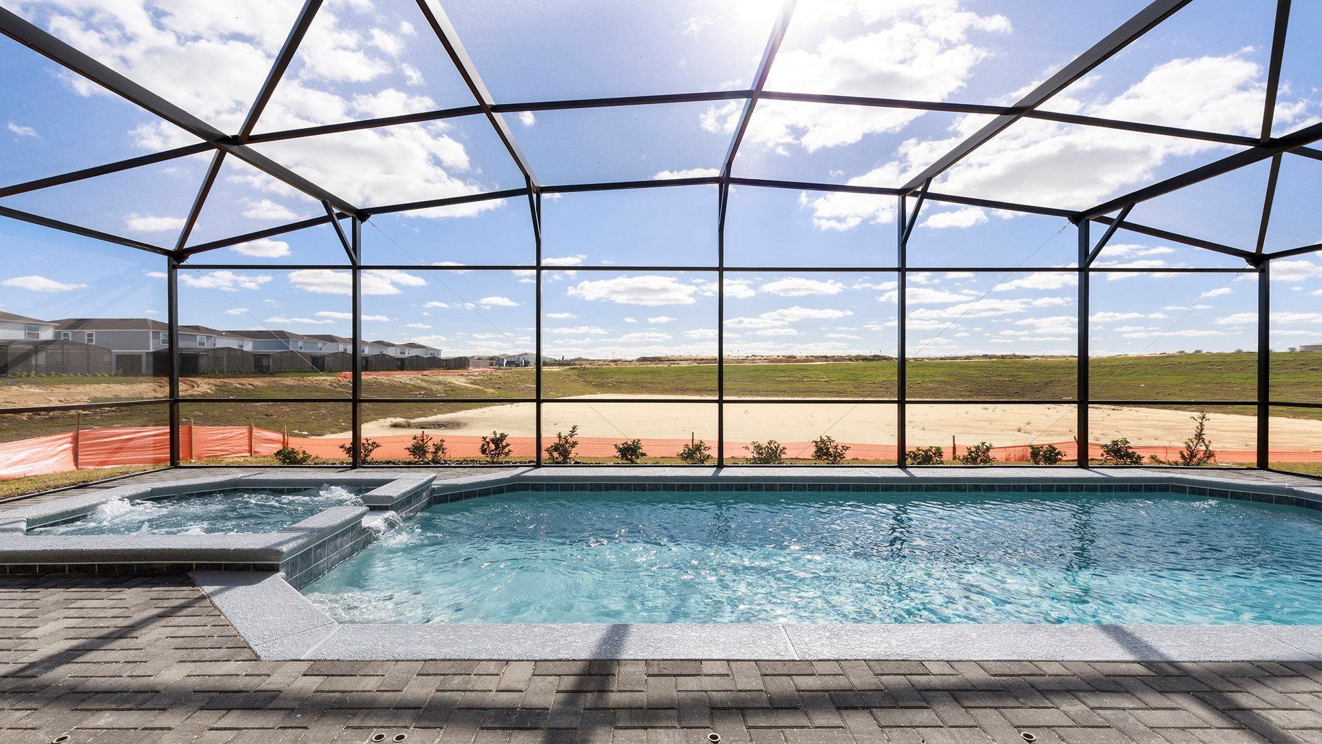 Screened-in pool and spa with sunny views of an open field and blue skies.