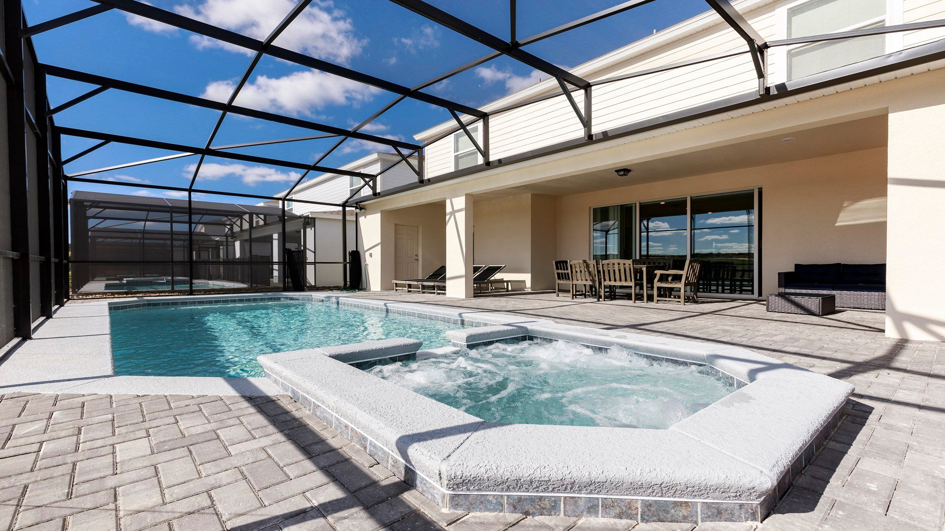 Spacious screened-in patio with a sparkling pool, hot tub, and outdoor seating.