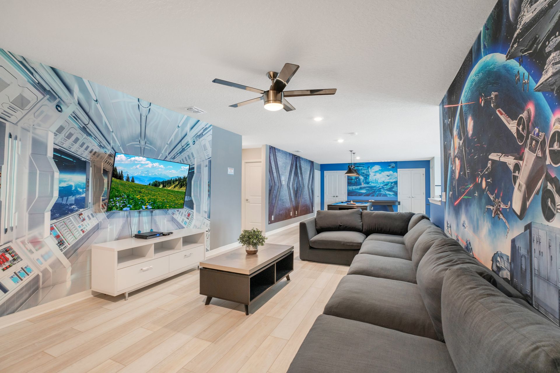 Futuristic-themed lounge with a cozy sectional, sci-fi murals, and a TV setup.