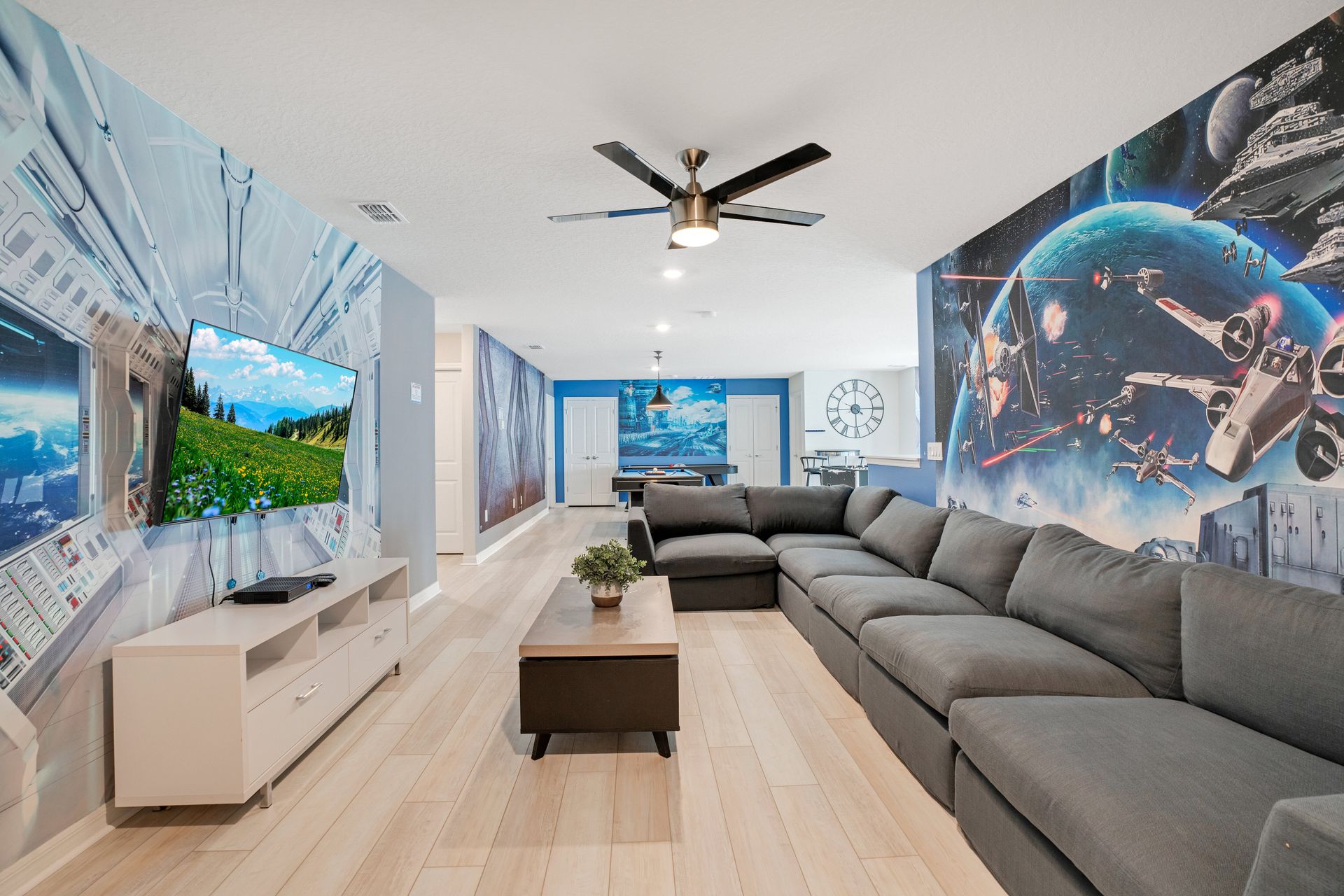Themed entertainment room with a large sectional, TV, and vibrant space murals.
