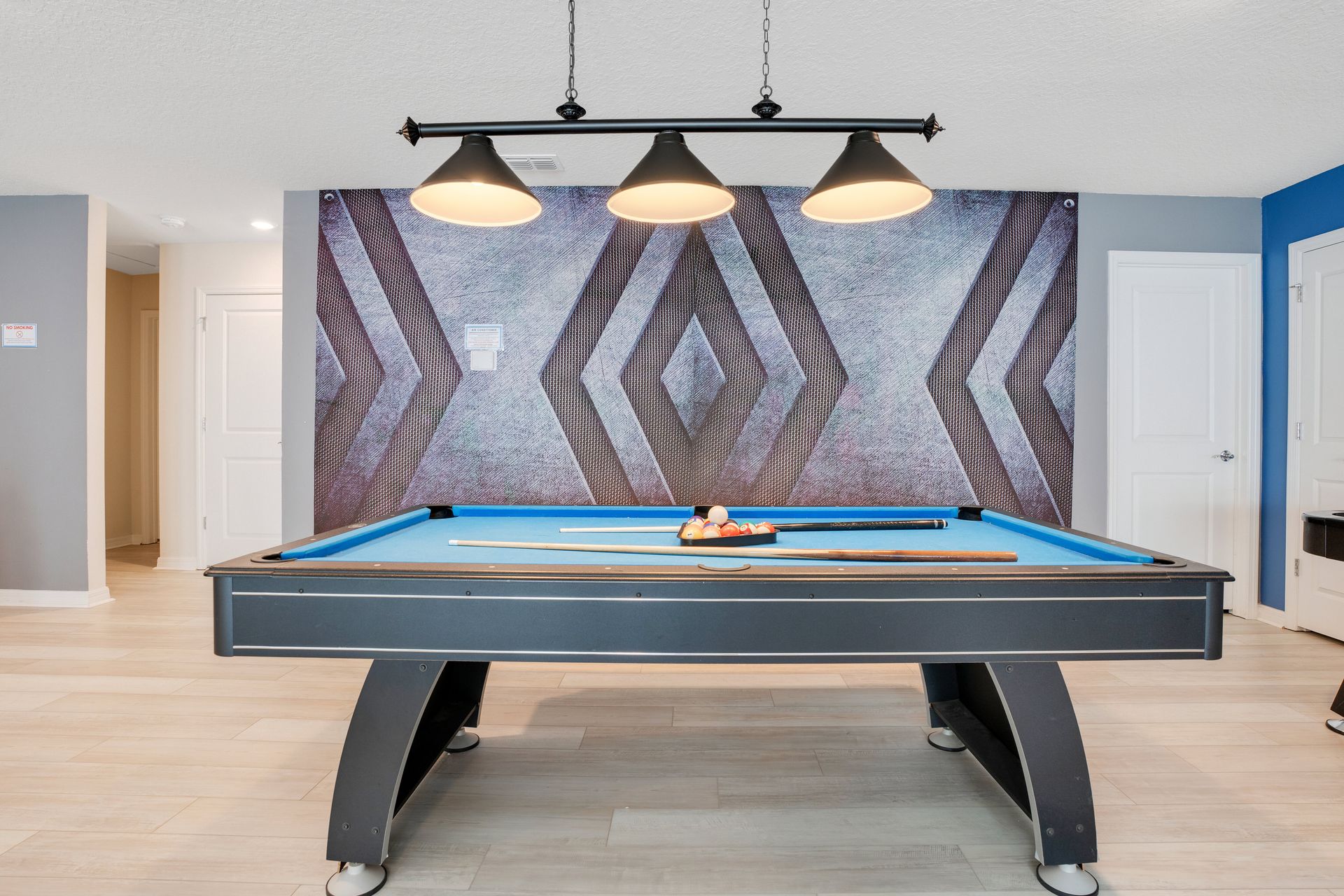 Modern game room with a sleek blue pool table and geometric accent wall.