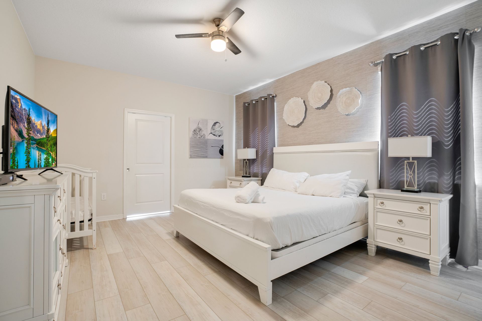 Modern master bedroom with elegant white furniture, soft gray accents, and a crib.