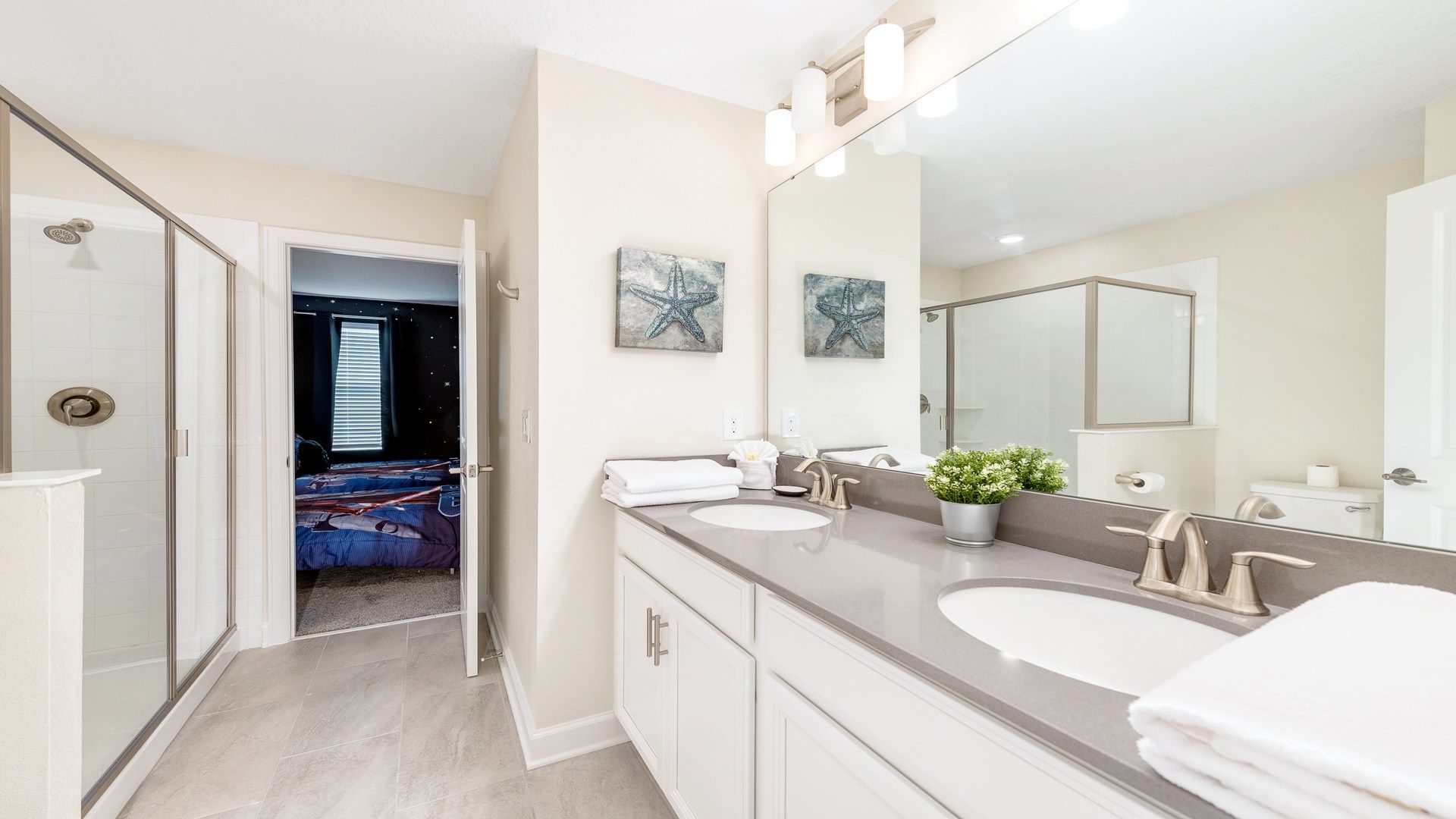 Bright bathroom with dual sinks, large mirror, and glass shower.