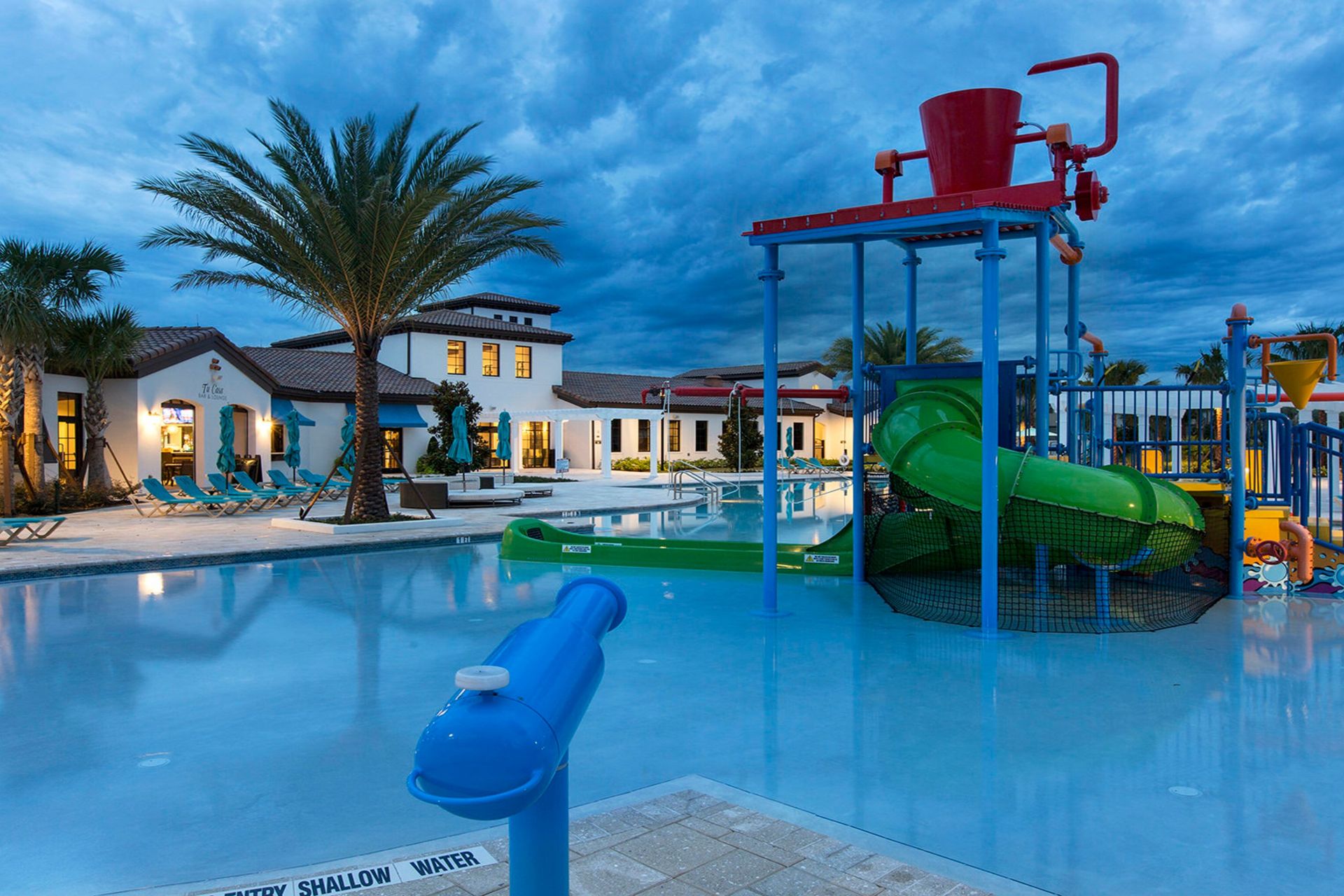 Evening view of the splash park with colorful slides, water cannons, and relaxing lounge areas under twilight skies.