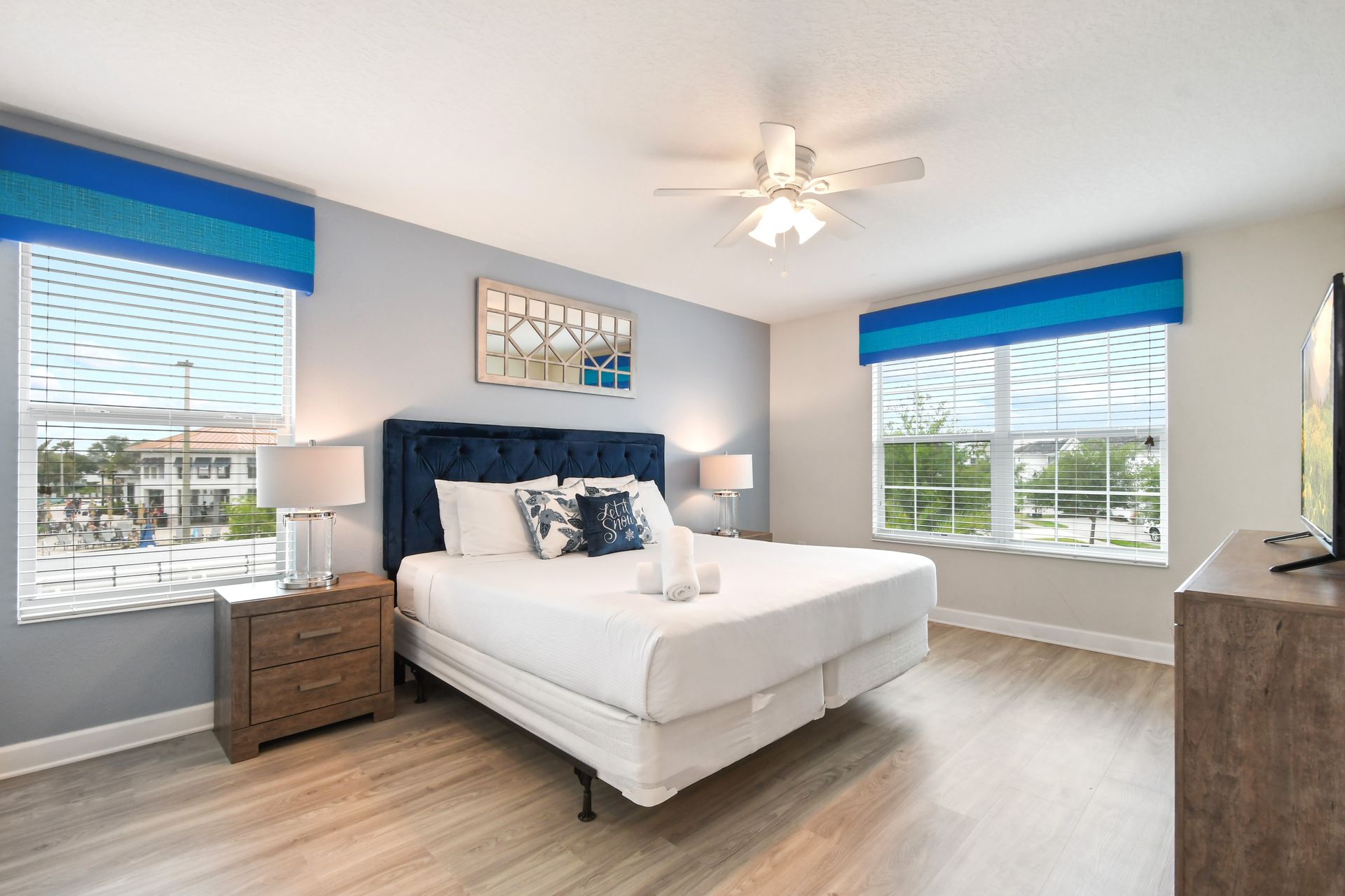 Spacious king bedroom with stylish blue accents, natural light, and a smart TV.