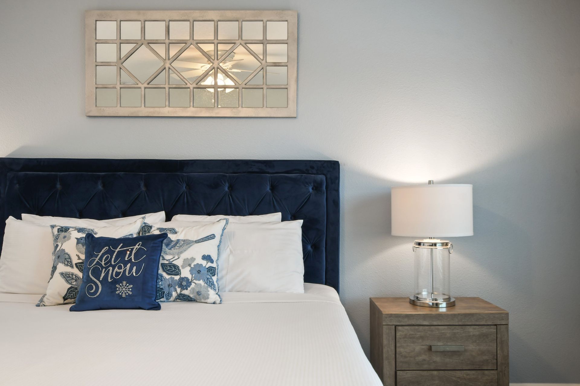 Chic and cozy bed setup with plush navy headboard and elegant mirrored decor.