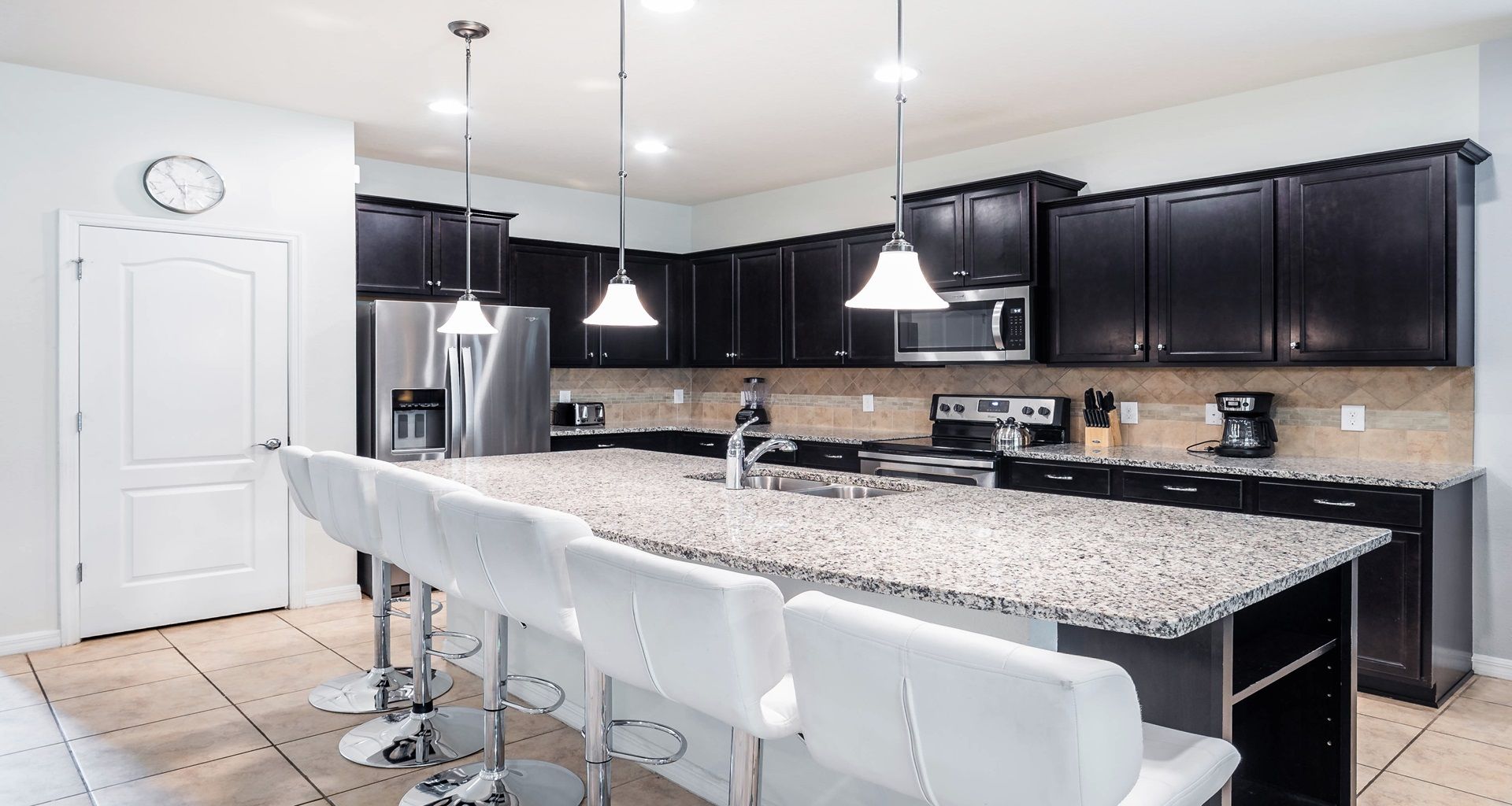 Fully equipped modern kitchen with granite counters and seating for six at island.