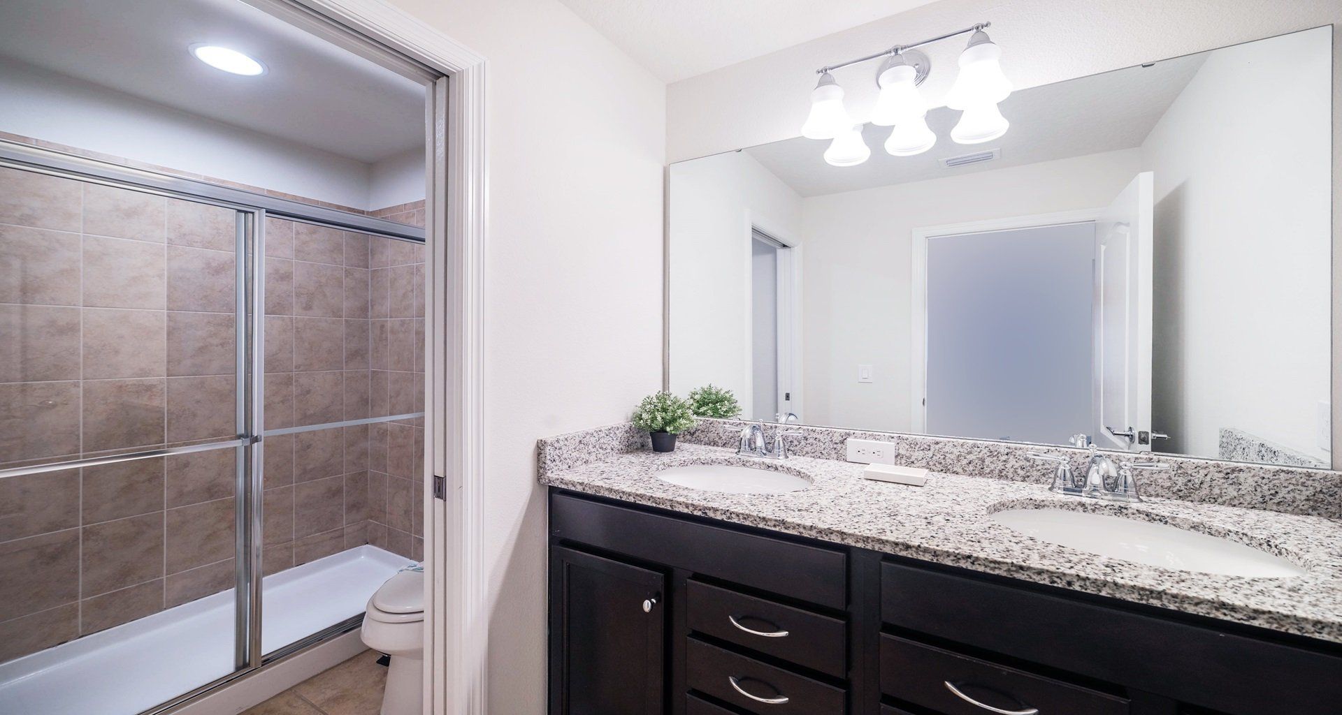 Sleek bathroom with granite double vanity, glass shower, and modern lighting.