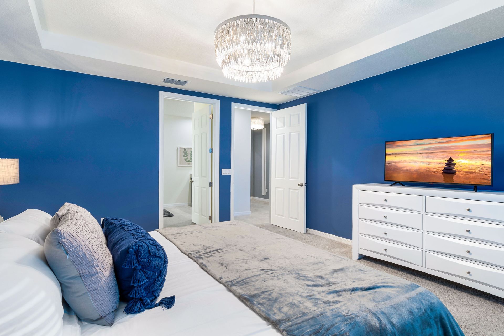 Luxurious bedroom with bold blue walls, plush bedding, and a chandelier!