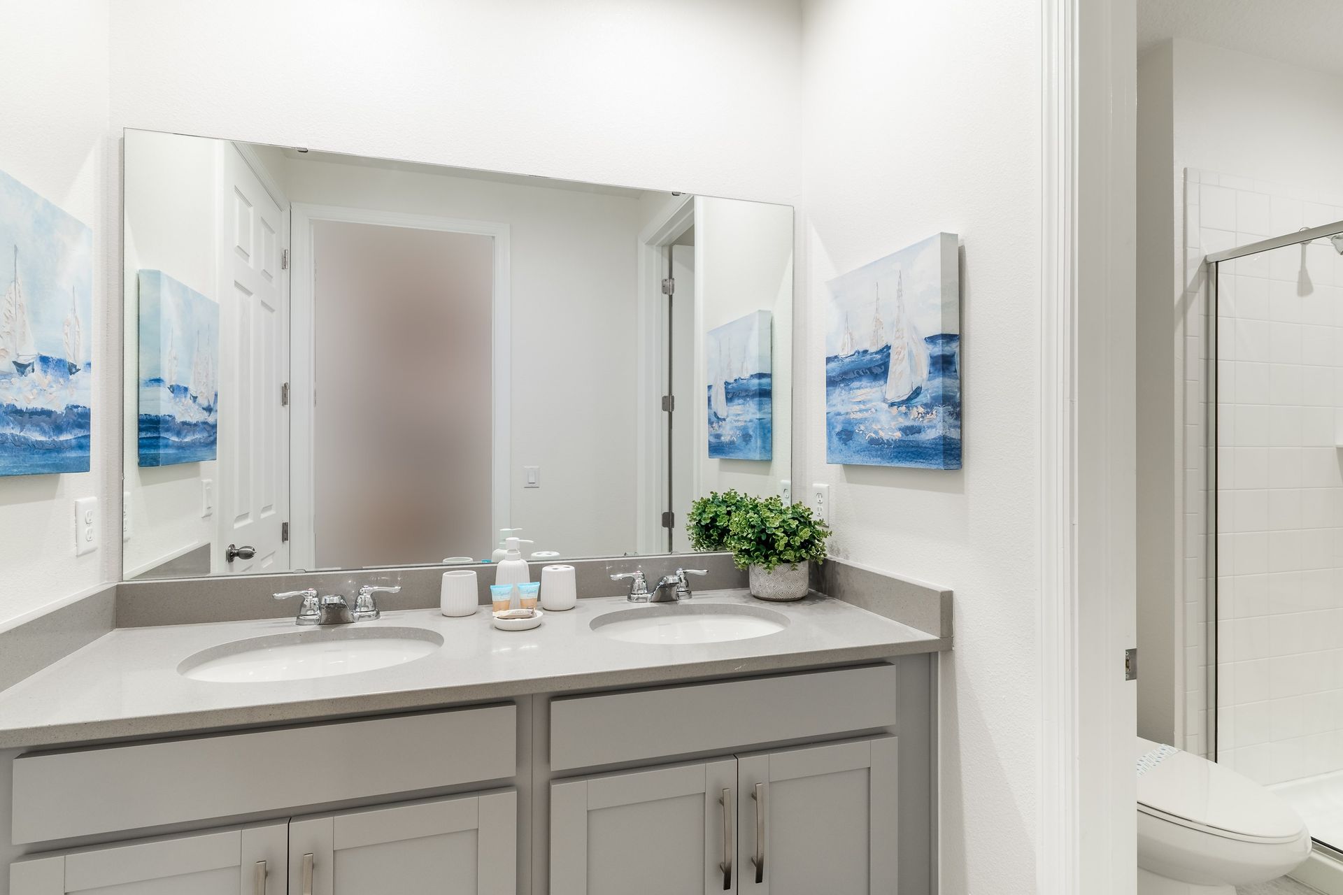 Bright bathroom with double sinks, modern shower, and coastal decor!