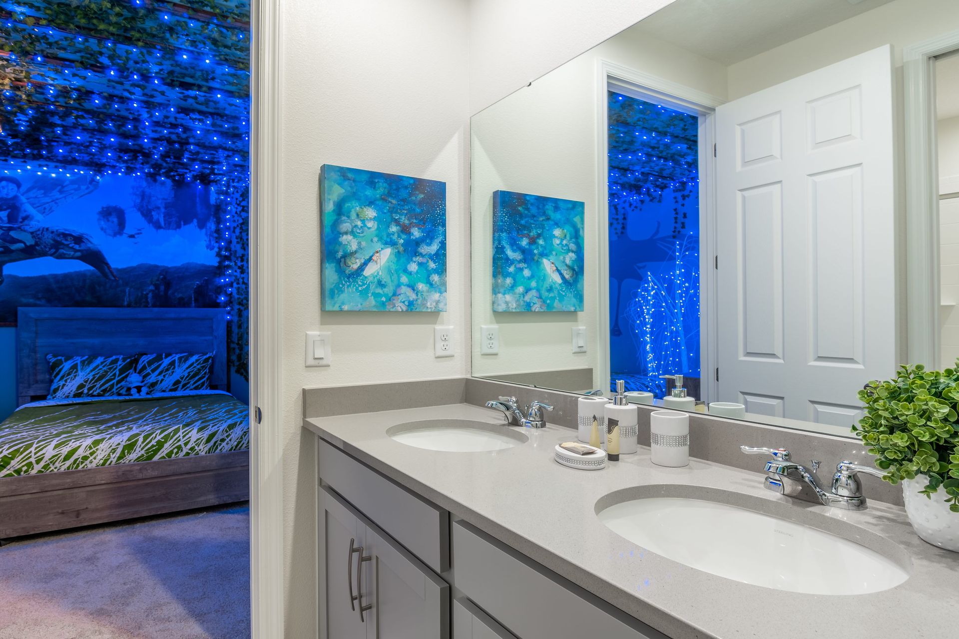 Elegant bathroom with dual sinks, vibrant art, and a view of a themed bedroom.