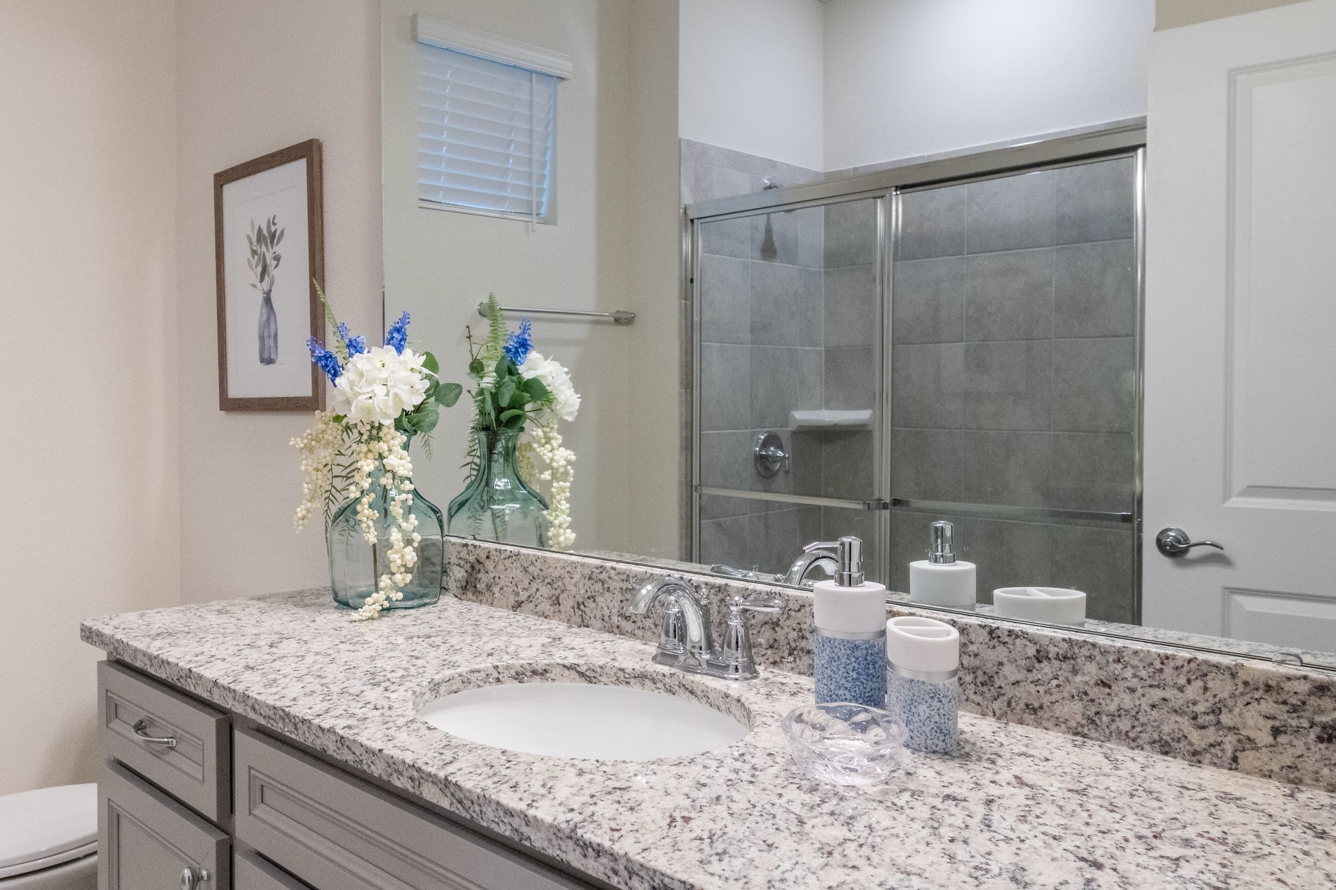 Modern bathroom with granite countertops, floral accents, and a spacious glass shower.