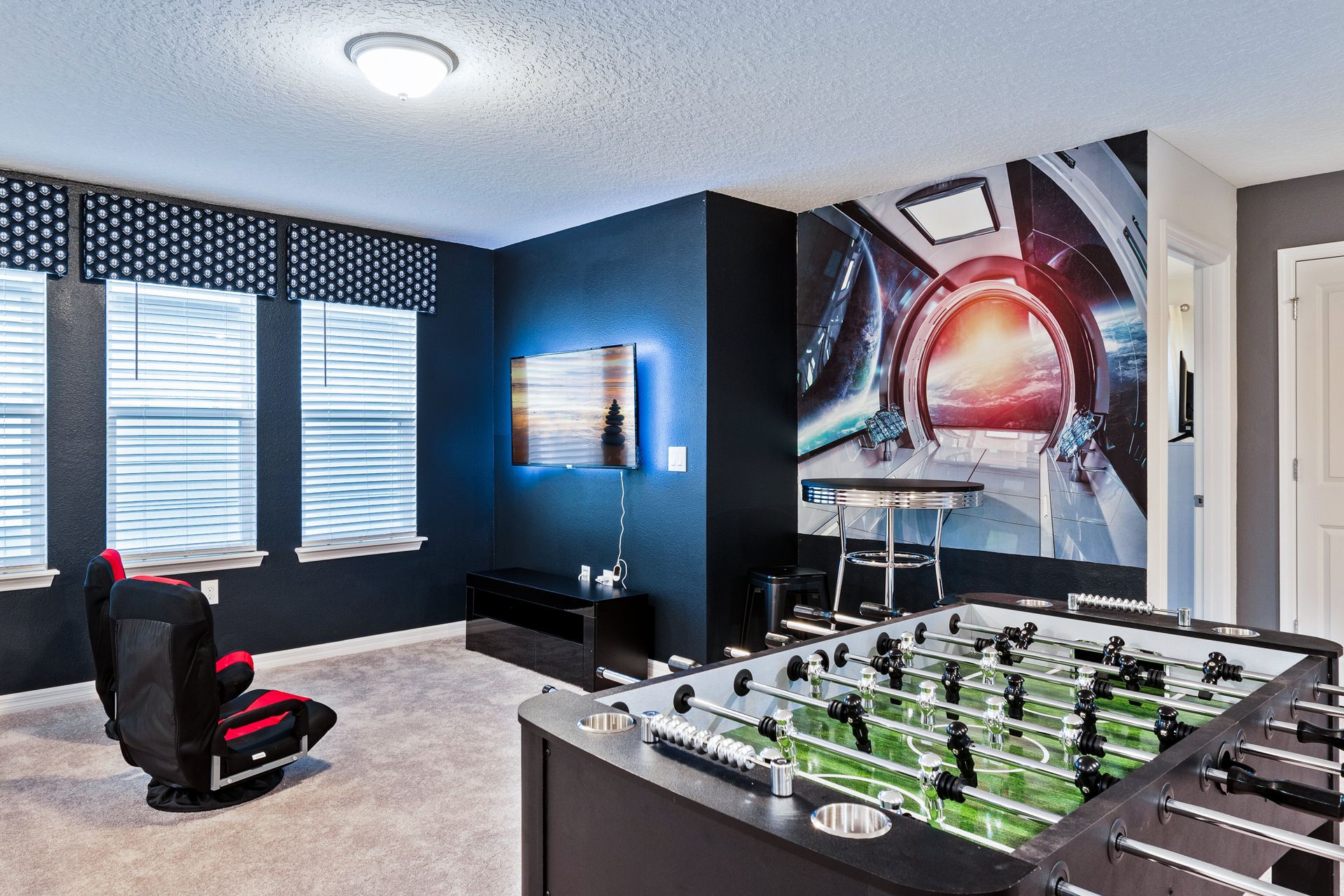 Space-themed game room with foosball, TV, and comfy gaming chairs.