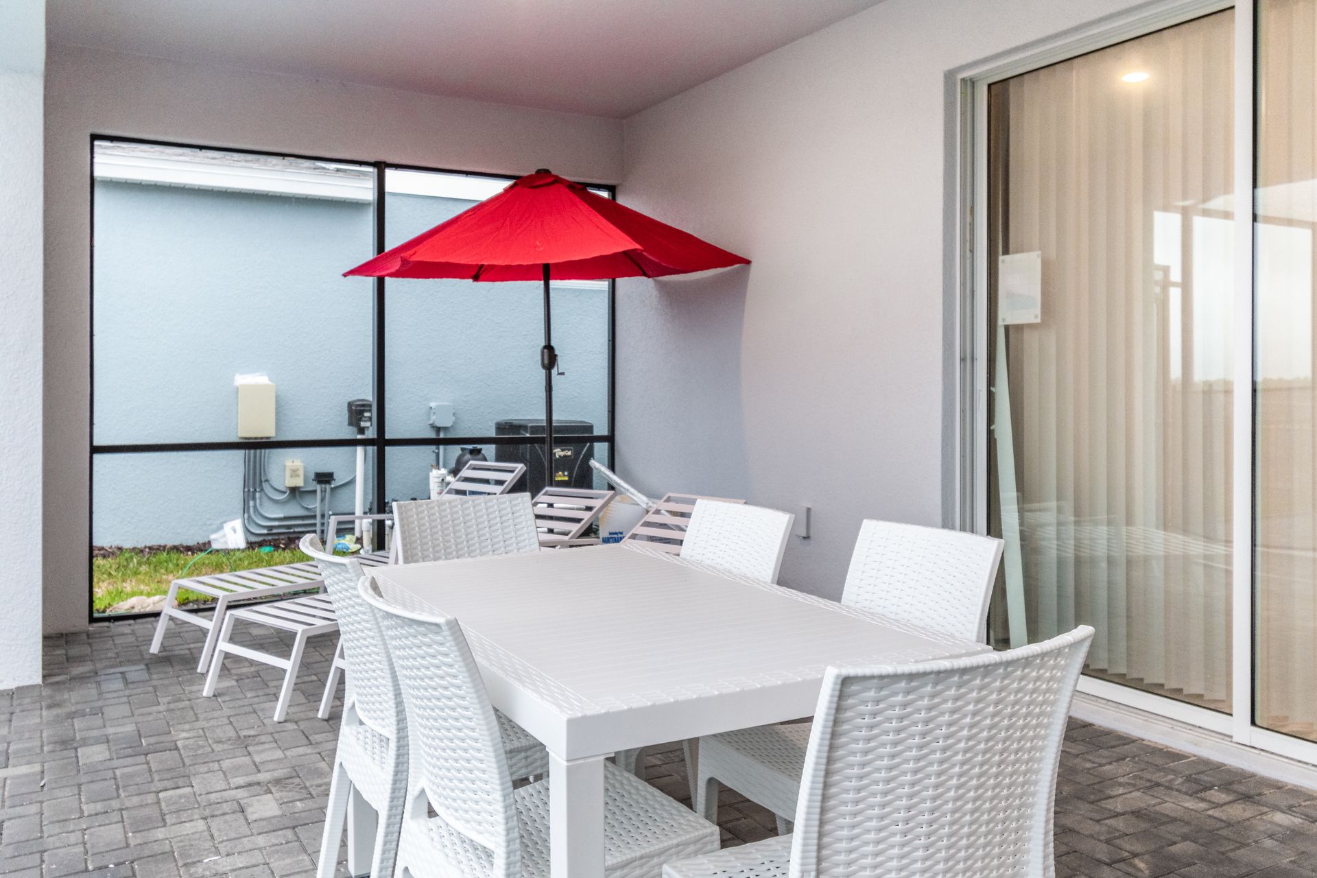 Outdoor dining area with white wicker furniture, shaded by a red umbrella.