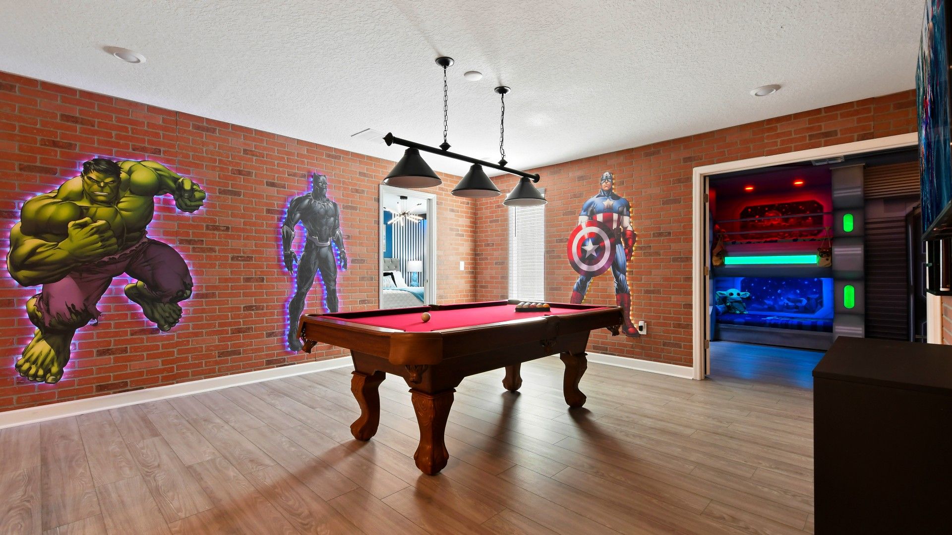 Superhero-themed game room with a pool table, brick accent walls, and bold décor.