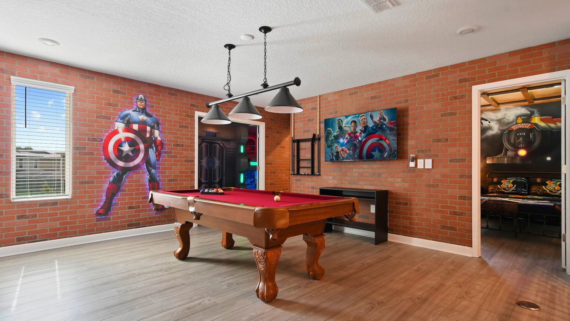 Superhero-themed game room with a pool table, brick accent walls, and bold décor.