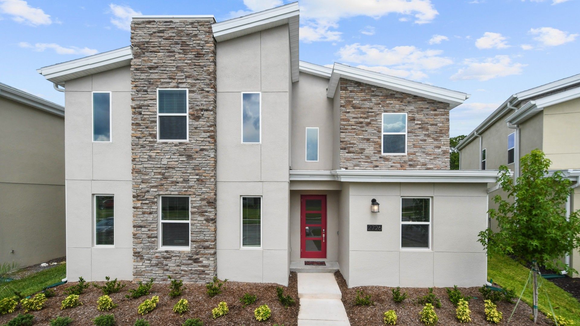 Modern luxury home with stone accents, stylish design, and a bold red front door.
