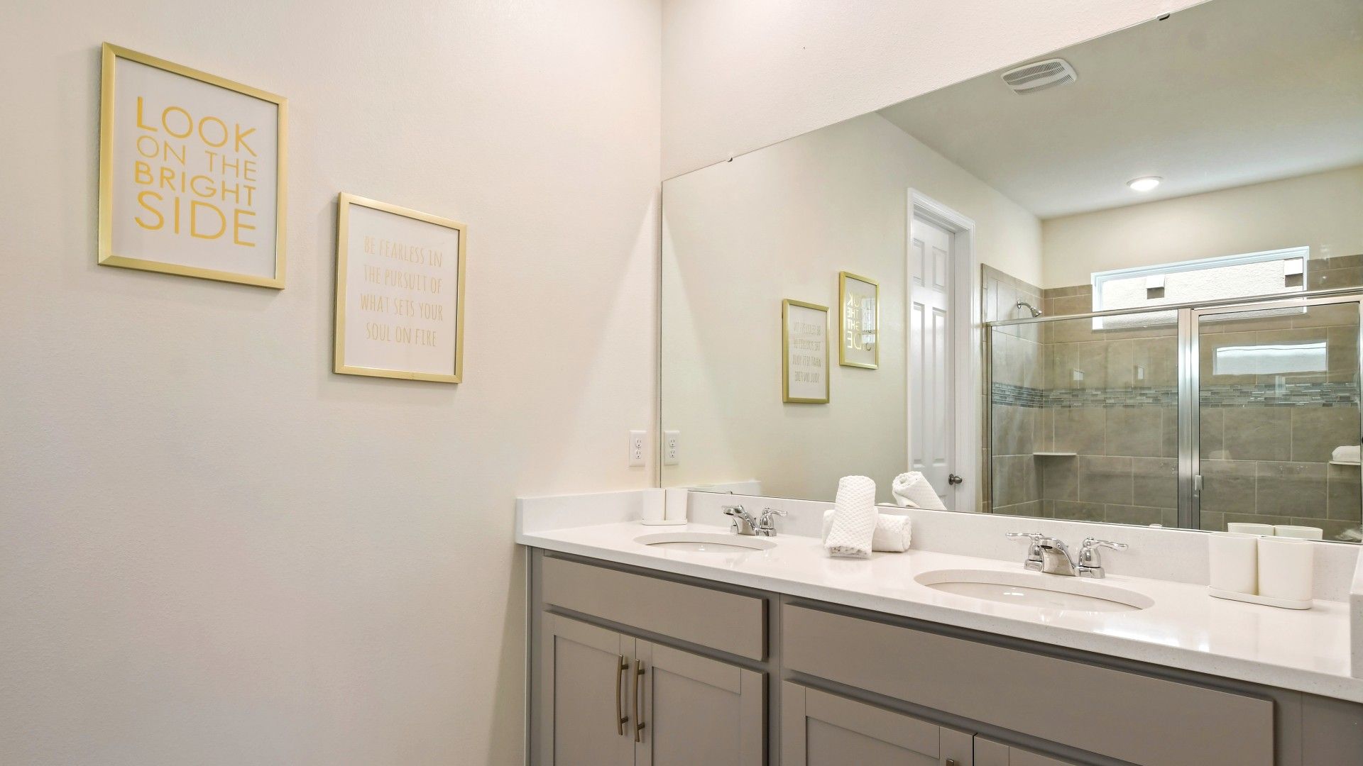 Bright, modern bathroom with dual sinks, glass shower, and uplifting decor.