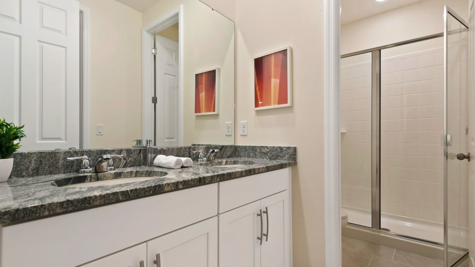 Modern bathroom with dual sinks, granite countertops, and a spacious glass-enclosed shower.