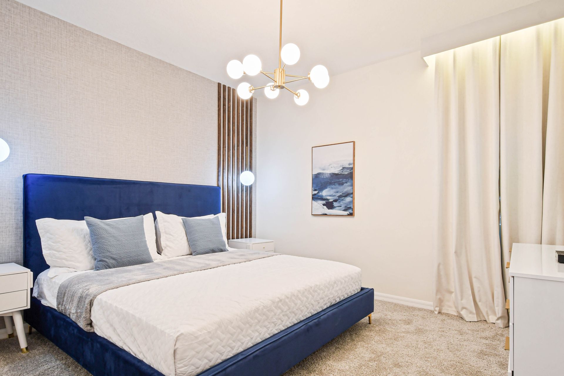 Chic bedroom with a plush blue bed, elegant lighting, and cozy decor.