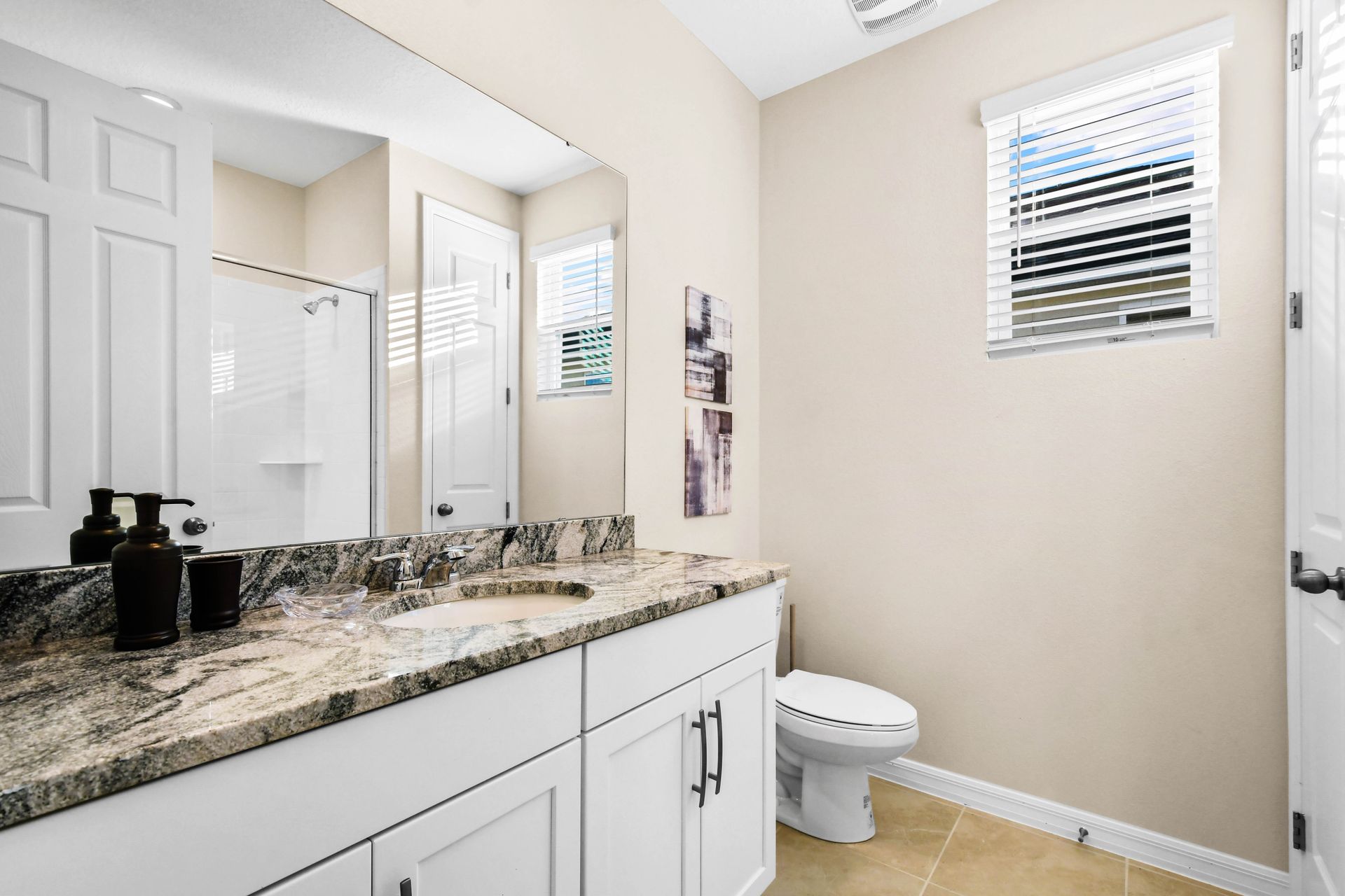 Modern bathroom with granite counters, bright window, and shower.