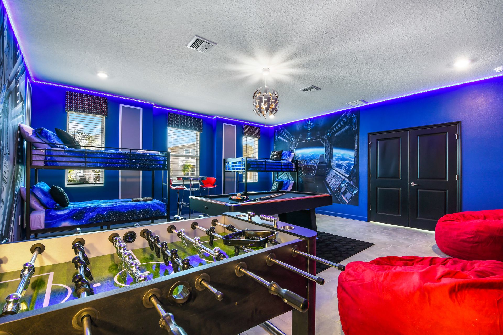 Galactic-themed game room with foosball, pool, bunk beds, and vibrant lighting.